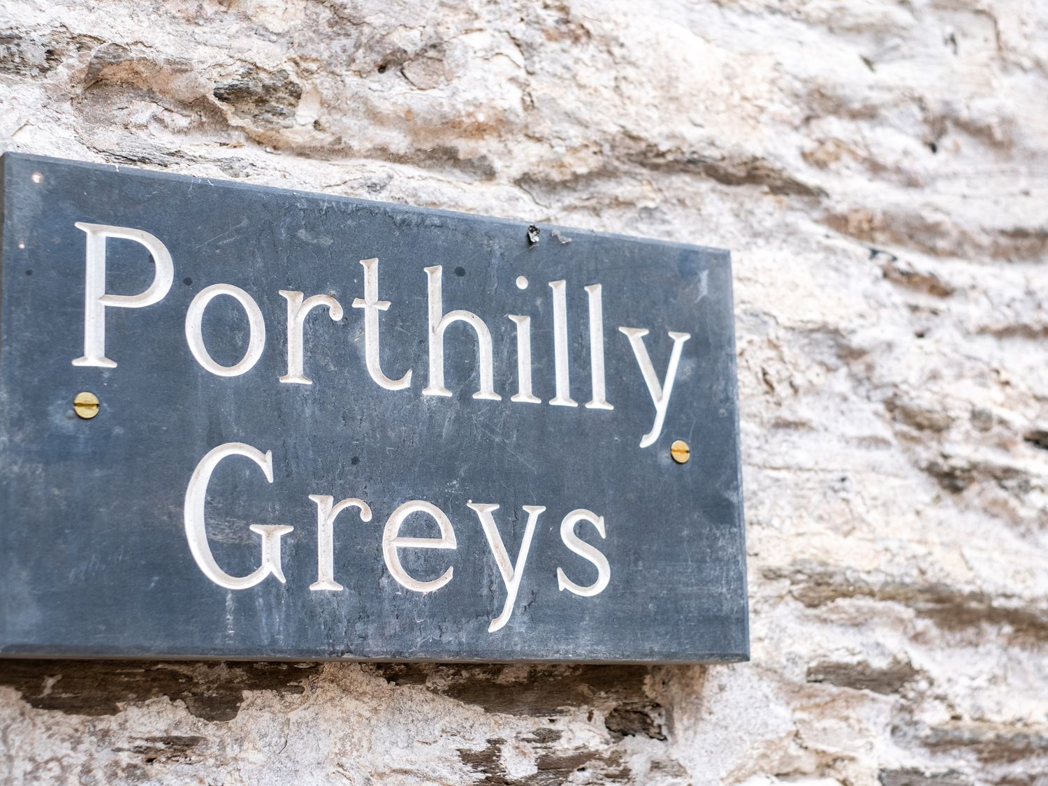 A stone wall with a black rectangular sign reading Porthilly Greys