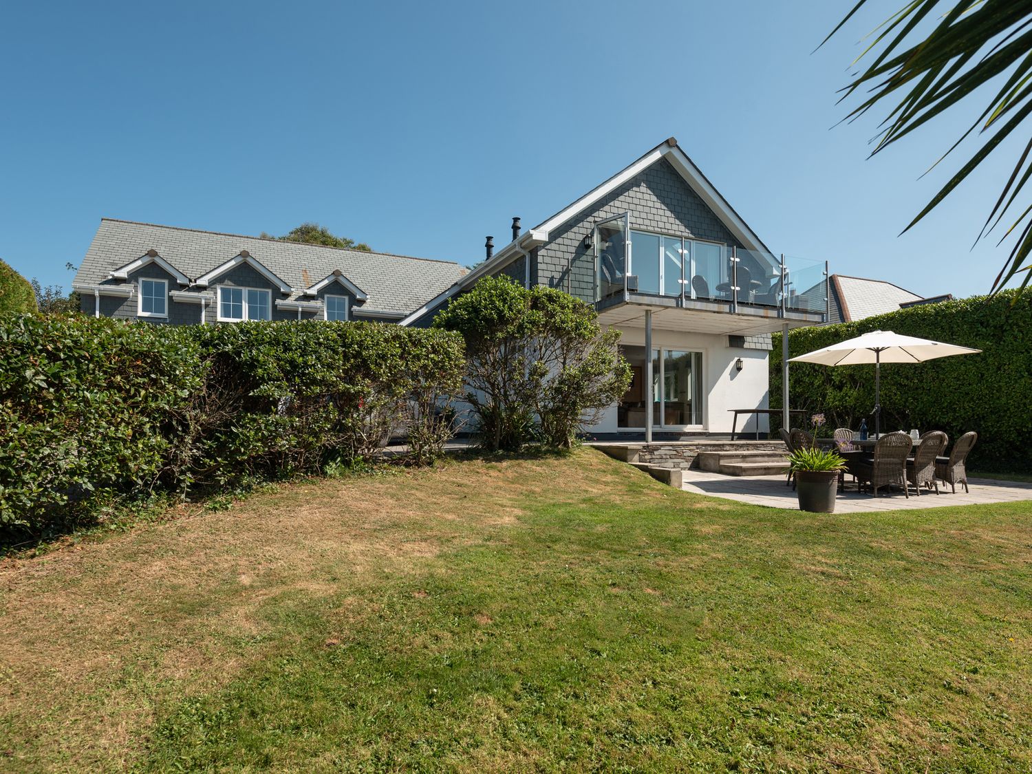A house with a balcony a garden with grass and a patio table with an umbrella at Farlands in Daymer Bay