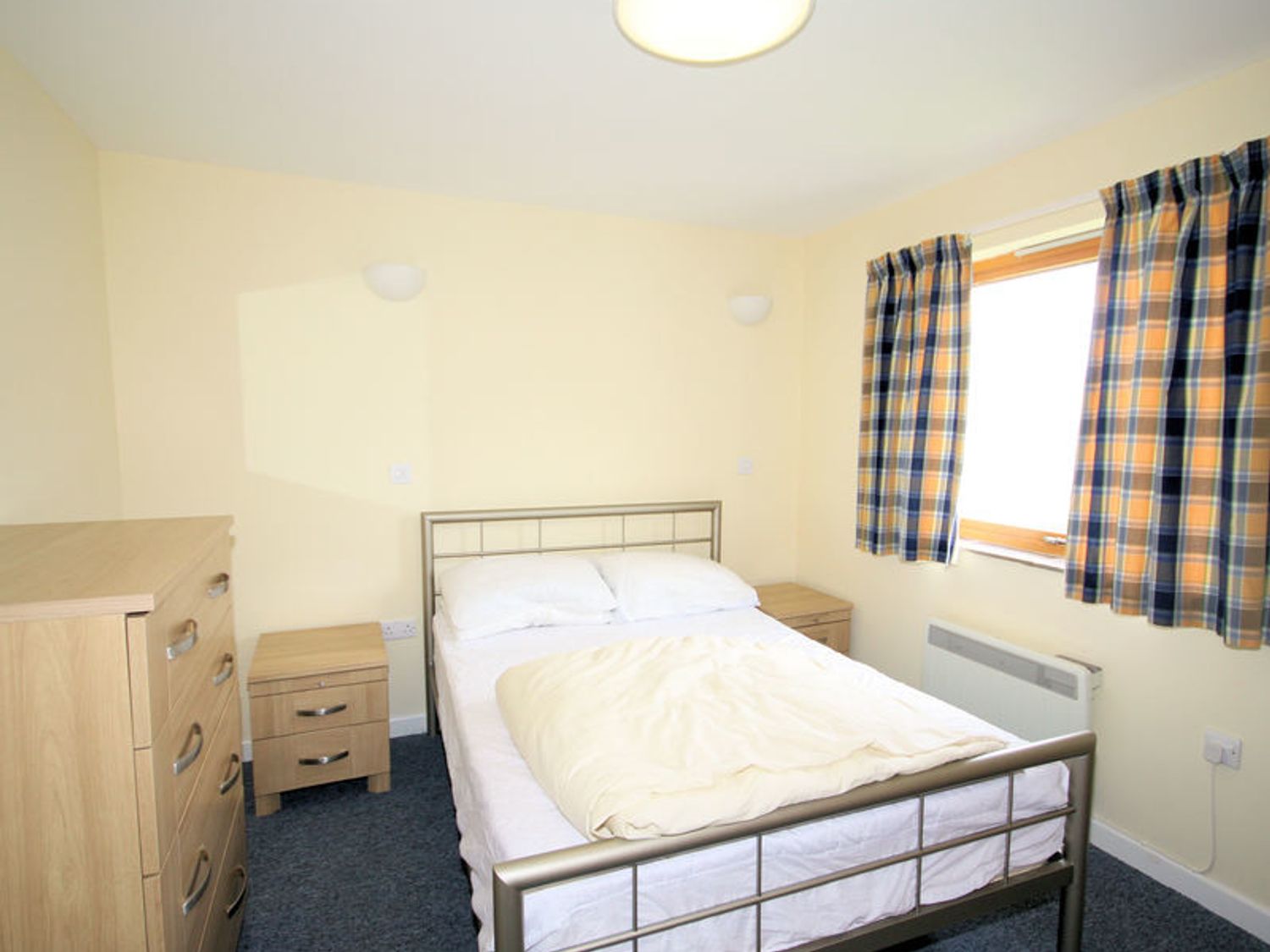 A bedroom with a metal bed frame dresser two bedside tables and a window with plaid curtains at Polzeath Court 4 in Polzeath