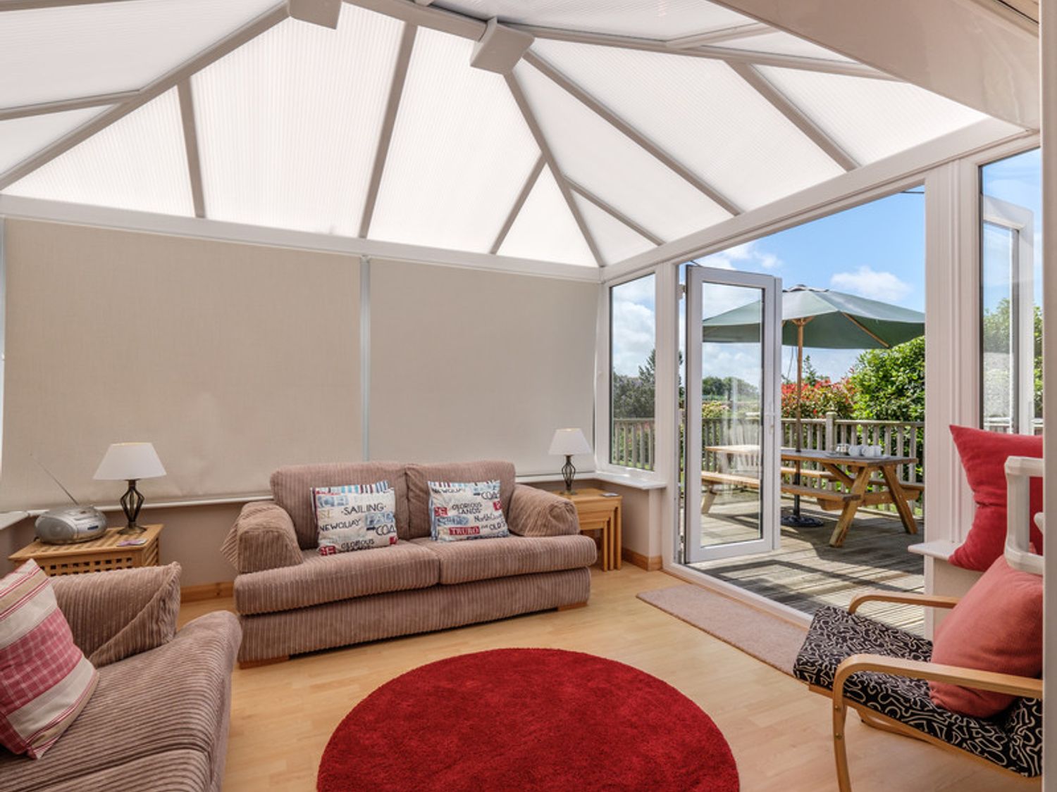 A conservatory with sofas and armchair around a round red rug and glass door leading to a patio at Cogenhoe in Rock