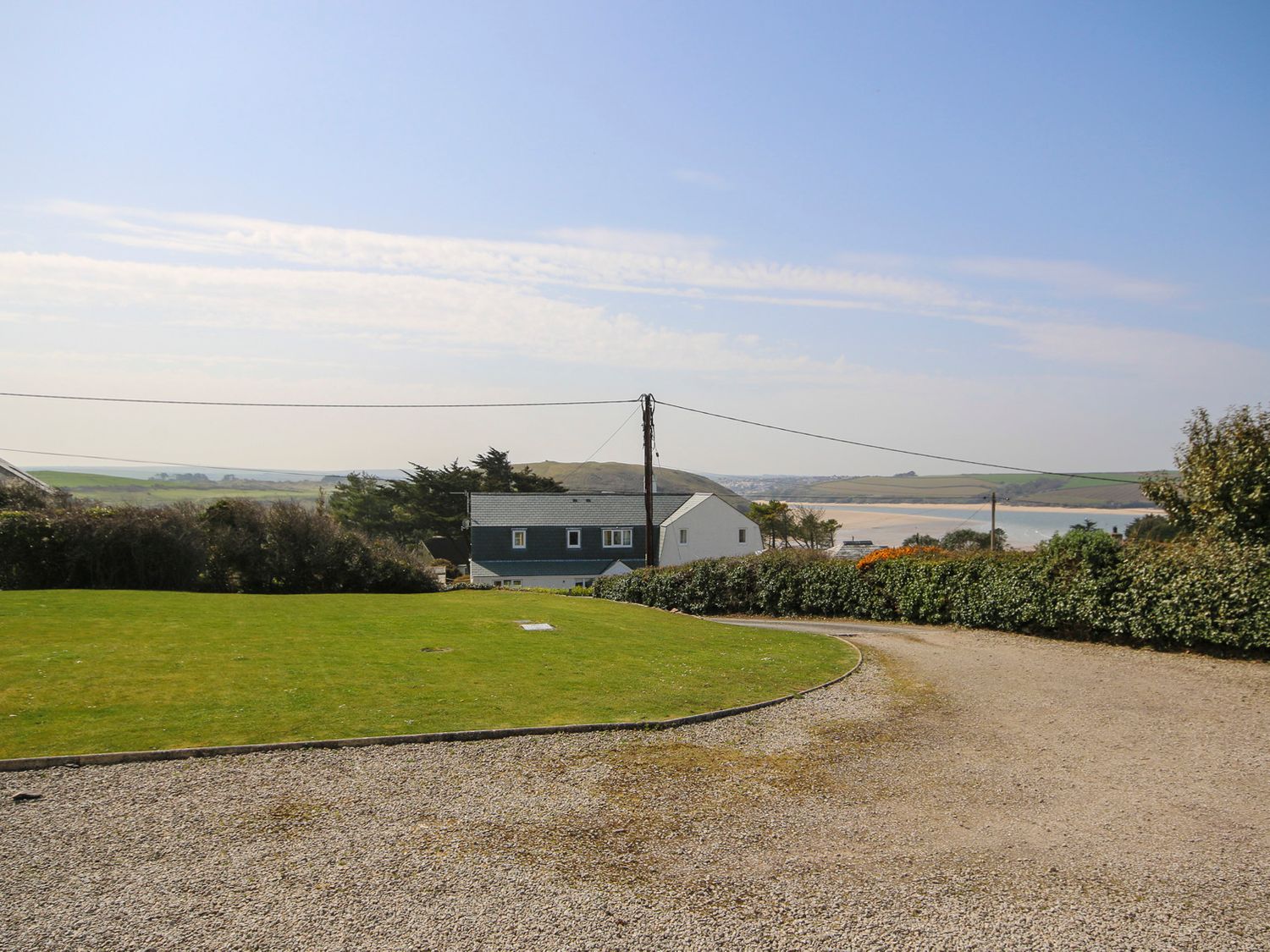 A gravel driveway and grassy area with houses and water in the background at Turnstones in Daymer Bay