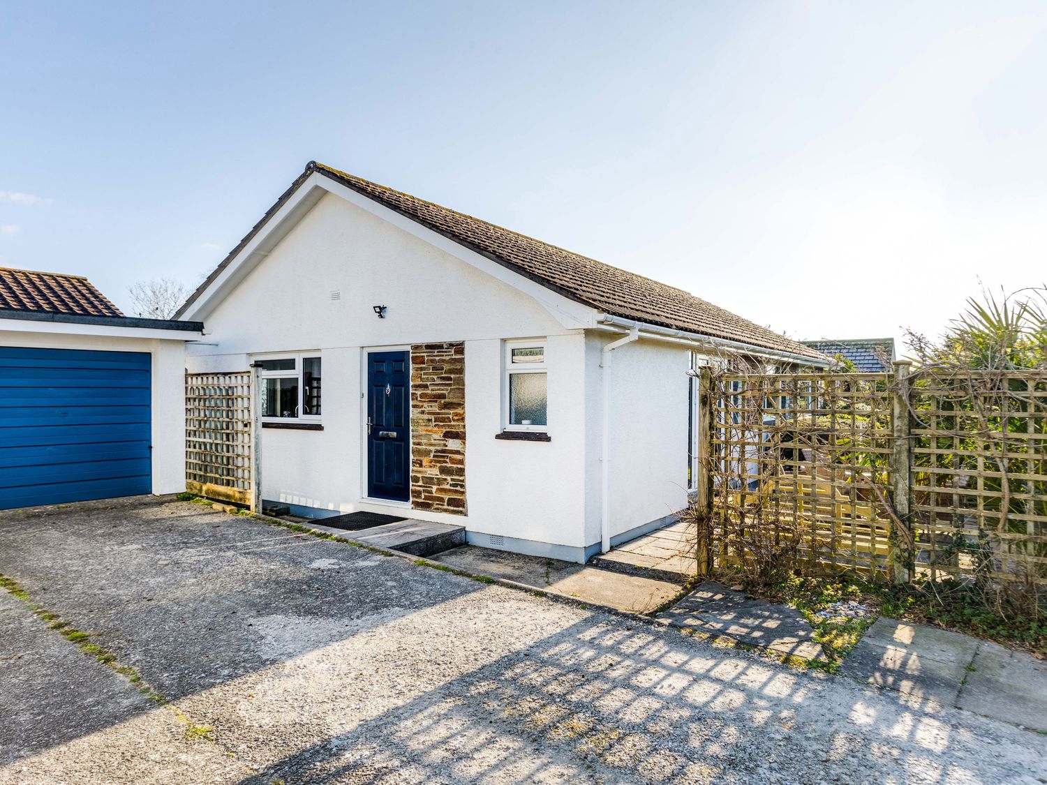 A white bungalow with a blue door and garage with trellis fencing in front at Little Sailing in Rock