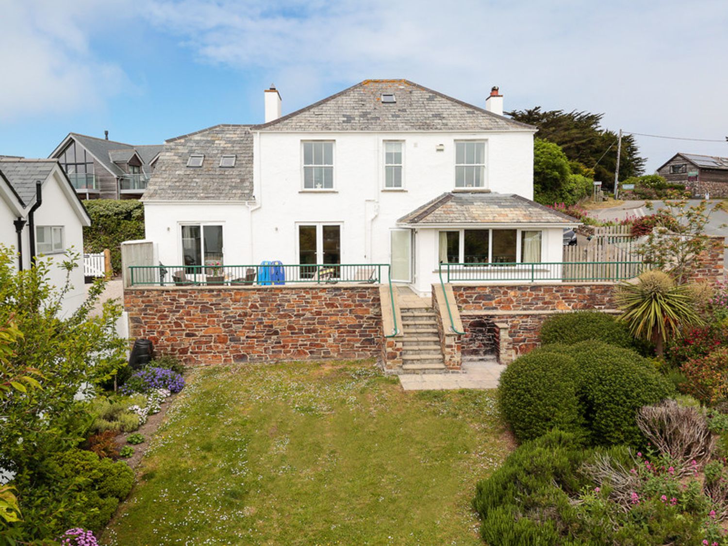 A white house with slate roof and stone terrace overlooking a garden at Worthy House in Daymer Bay
