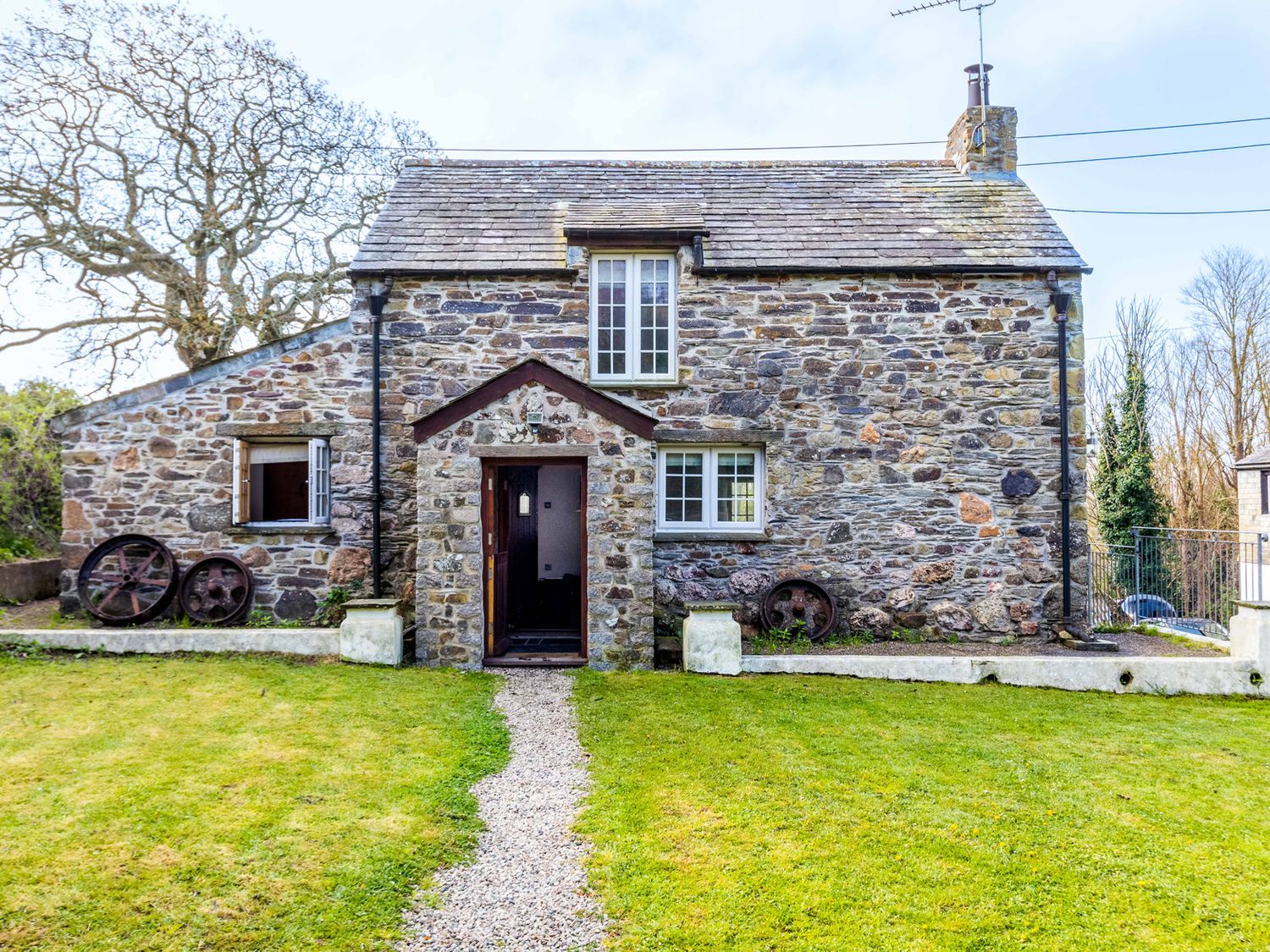 A stone cottage with a gravel path leading to an open wooden door and lawn at Dingles Cottage in Rock