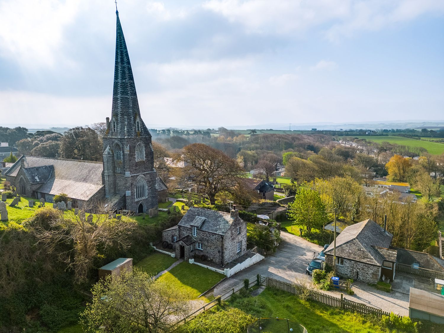 A stone church with a tall steeple next to stone houses and trees in a rural village