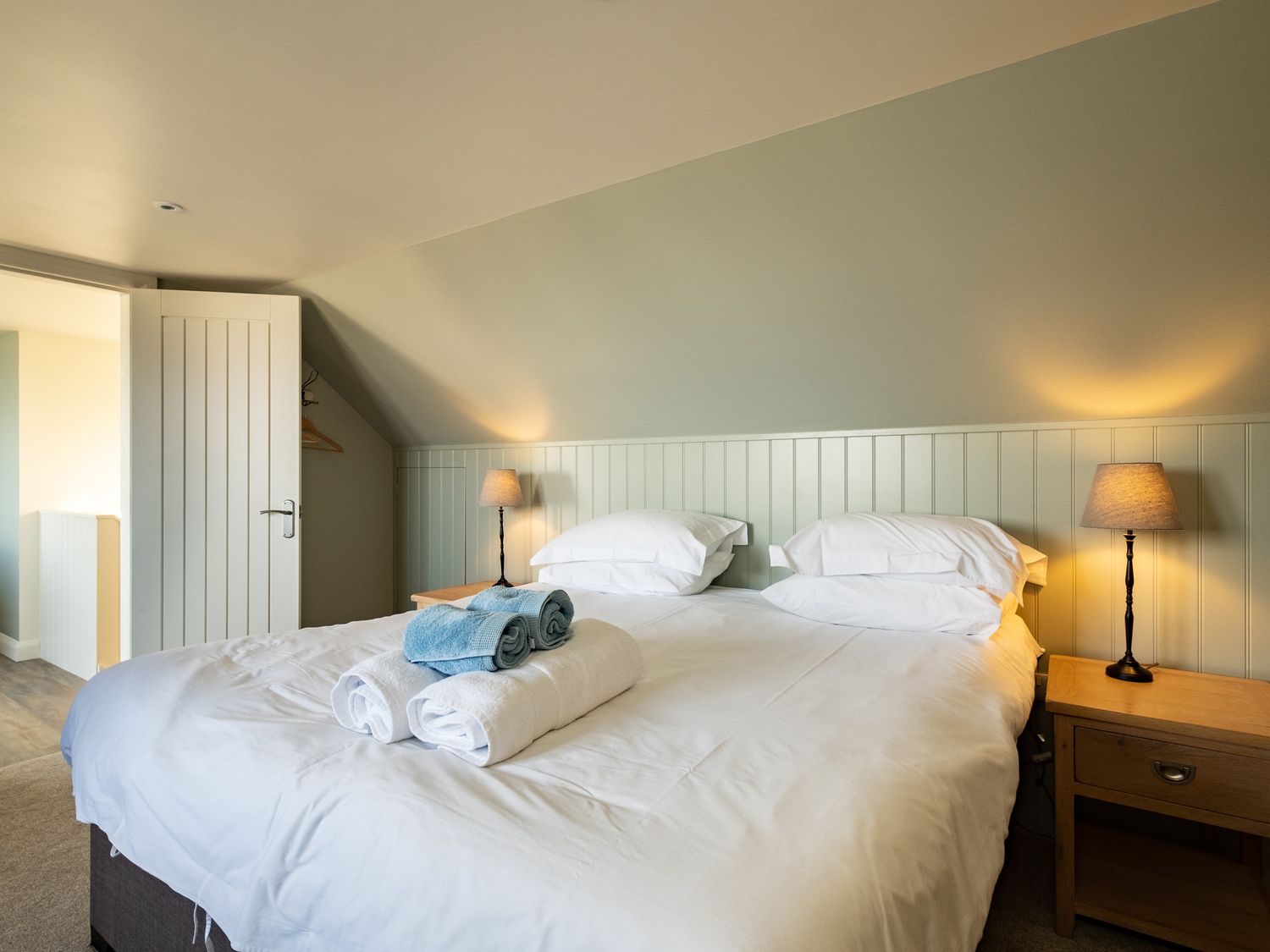 A bedroom with a double bed white linens two bedside tables with lamps and folded towels on the bed at Atlantis in Polzeath