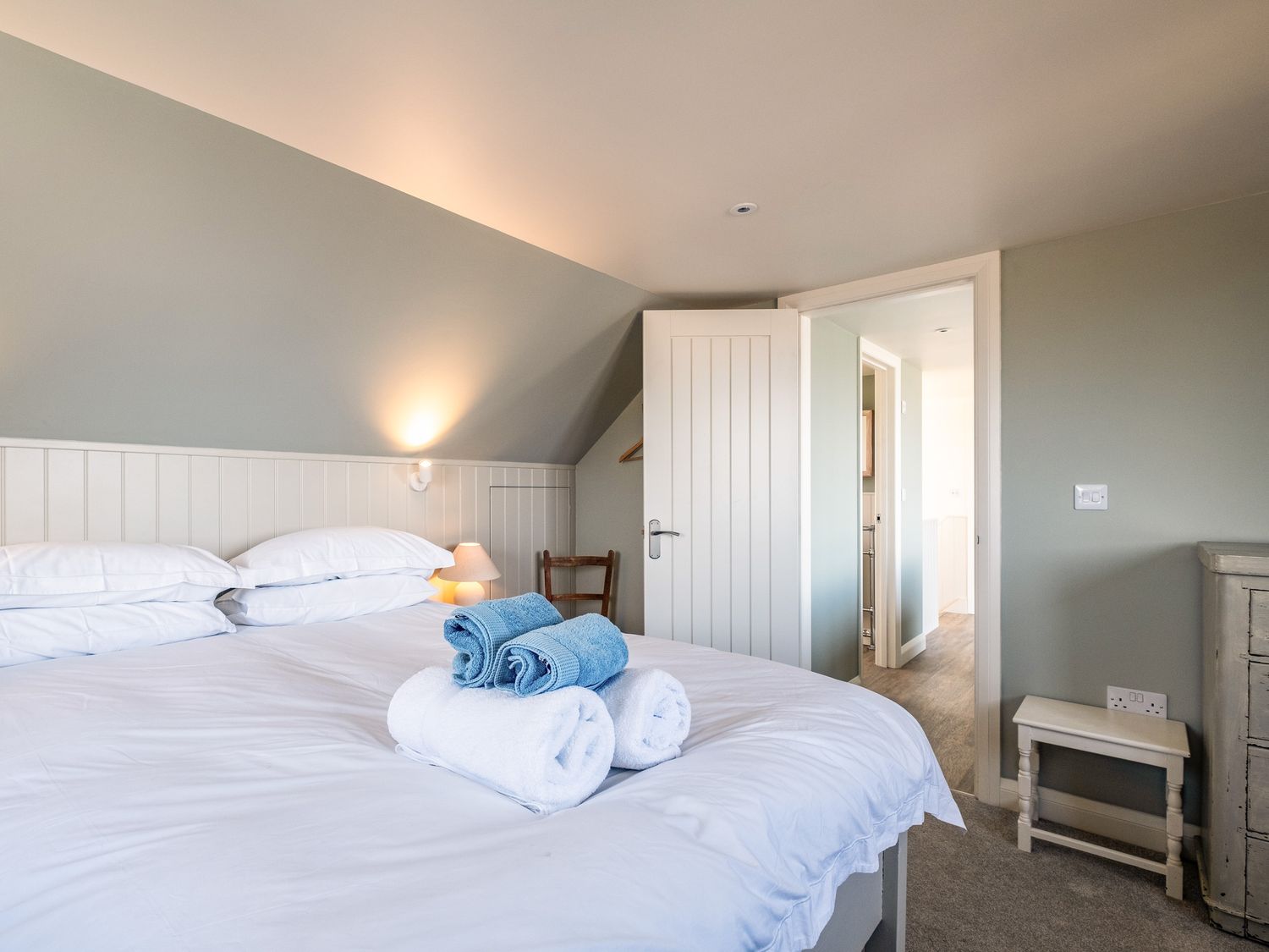 A bedroom with a bed with white linens and folded towels on top and a door opened to a hallway at Atlantis in Polzeath