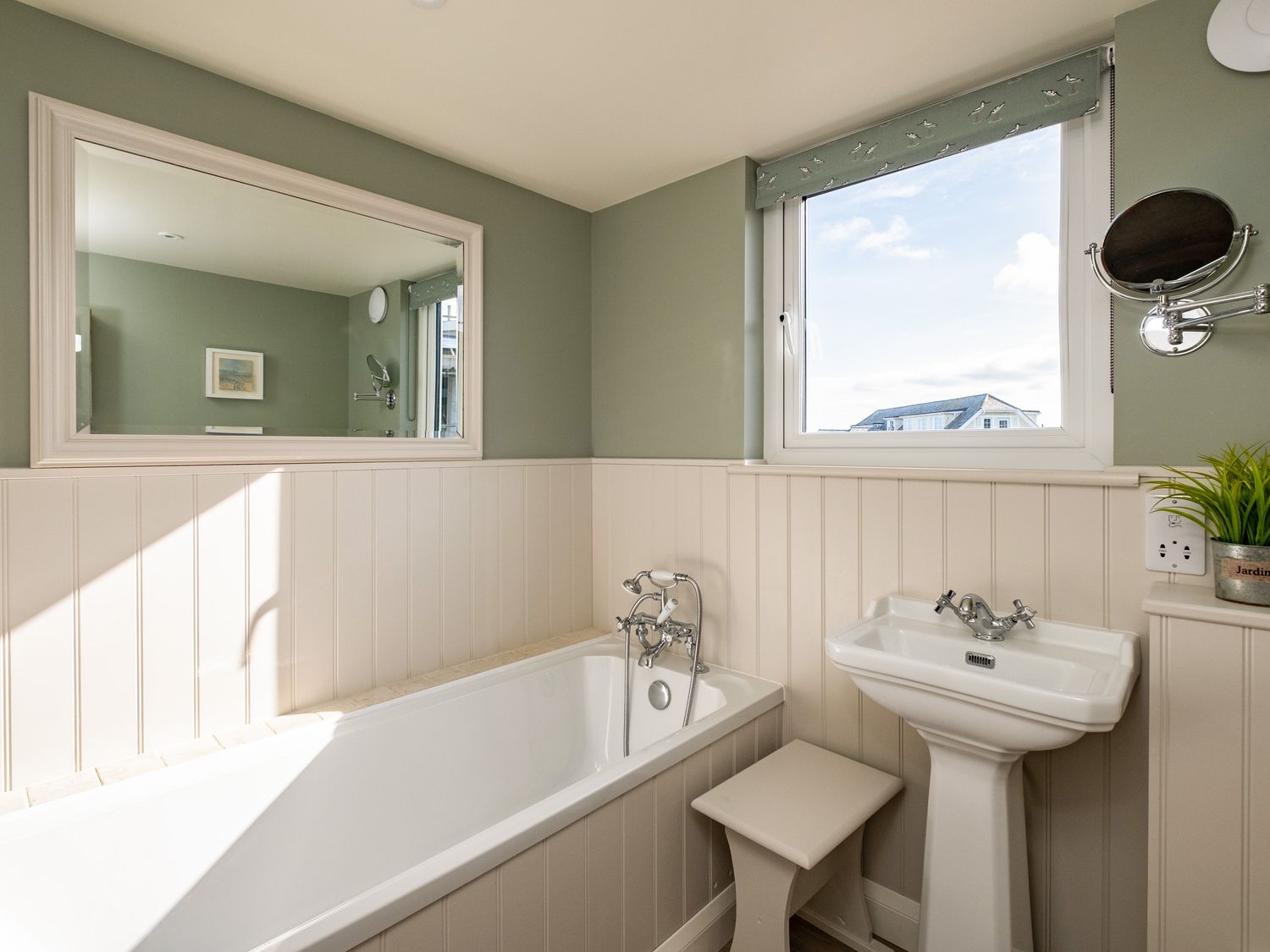 A bathroom with a bathtub sink mirror window and small stool at Atlantis in Polzeath