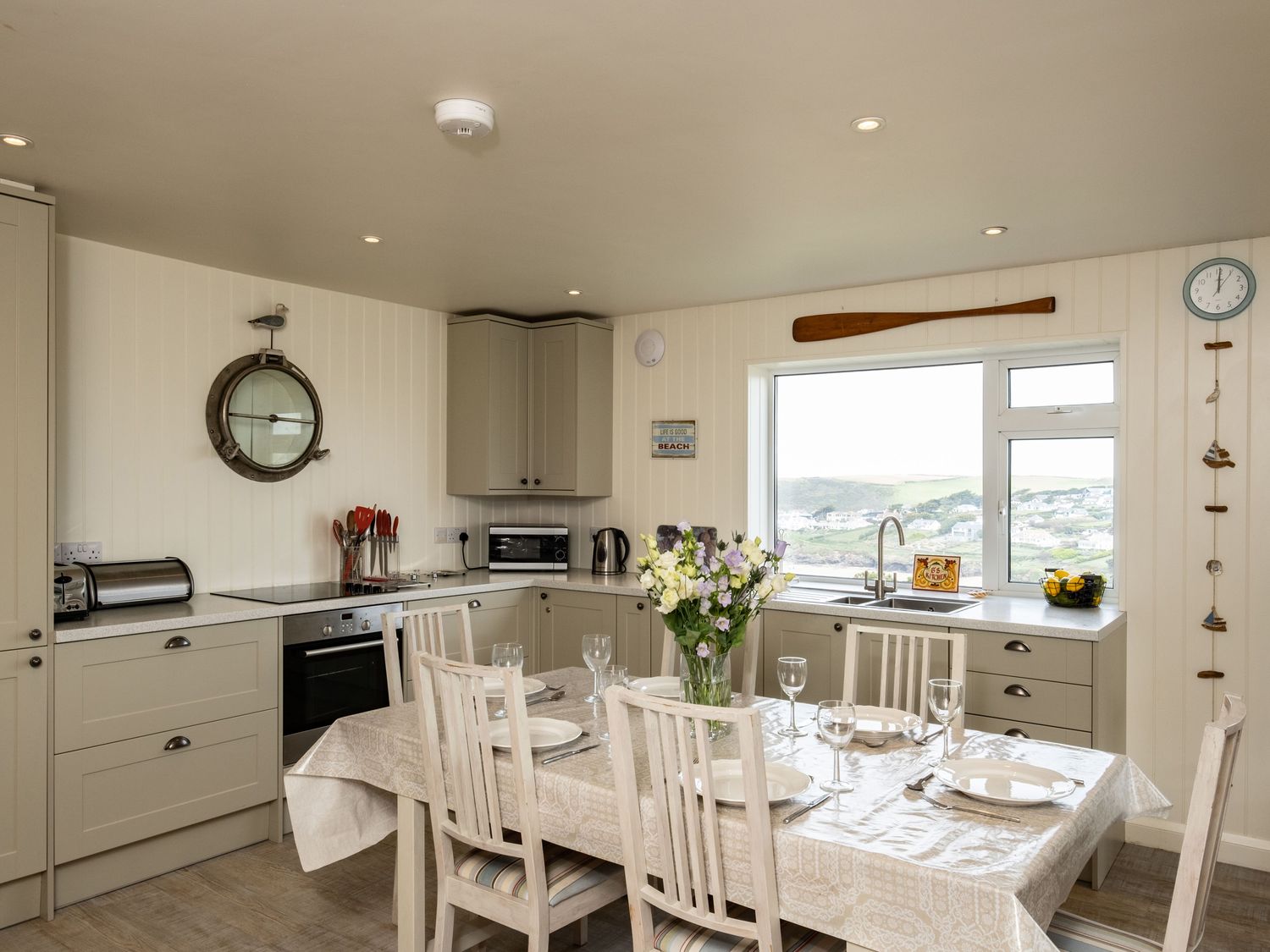 A kitchen with a dining table set with plates and glasses and a window with a view at Atlantis in Polzeath