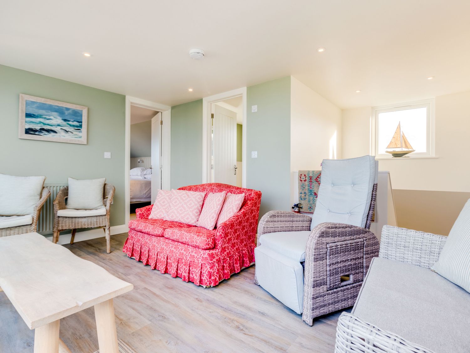 A sitting room with a red loveseat a wicker armchair a grey armchair and a wooden coffee table at Atlantis in Polzeath