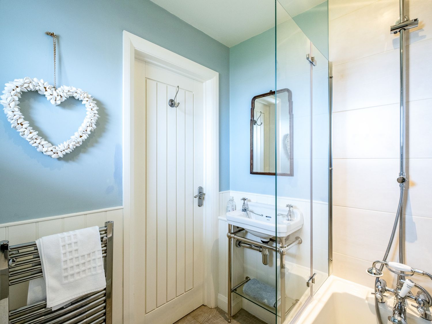 A bathroom with a heart-shaped wall decoration a towel rack a sink and a shower area at Atlantis in Polzeath