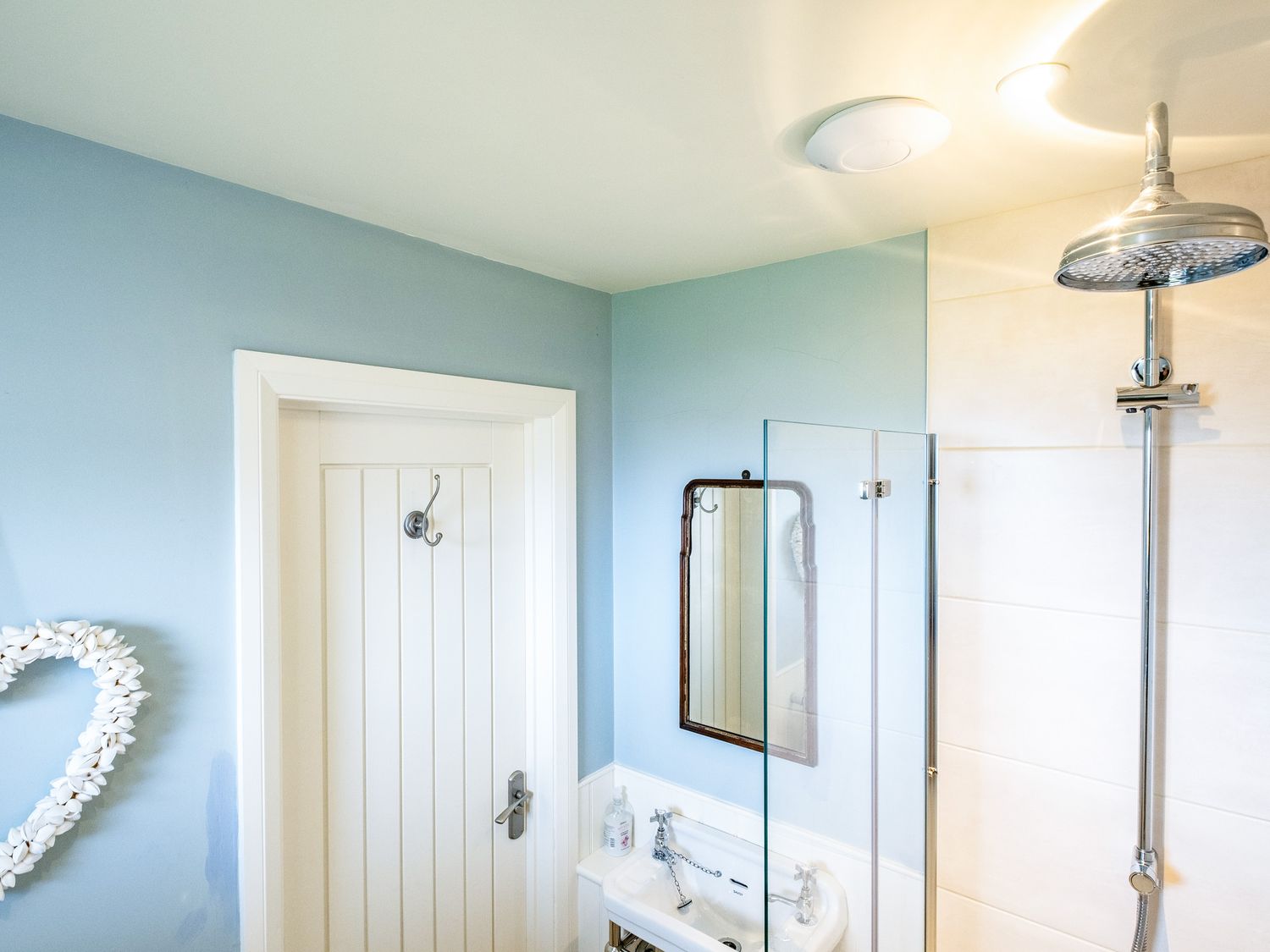 A bathroom with a shower head sink mirror and a white door at Atlantis in Polzeath