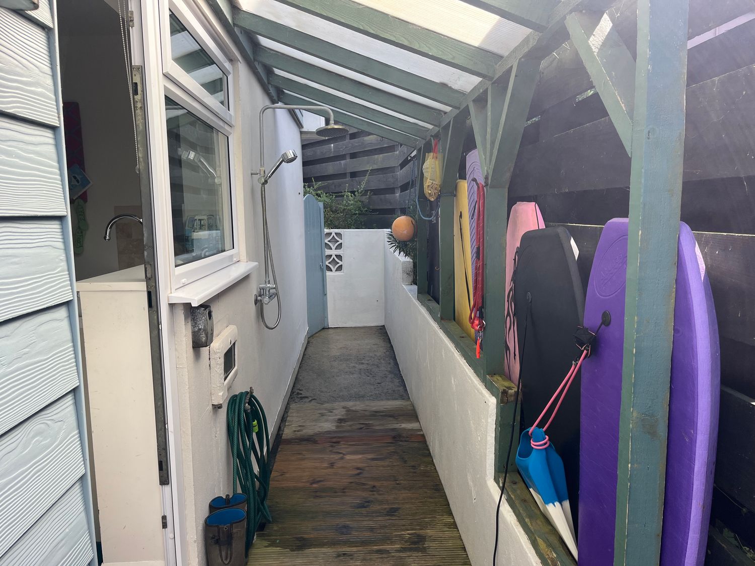 A covered outdoor corridor with an outdoor shower and bodyboards hanging on the wall at Atlantis in Polzeath