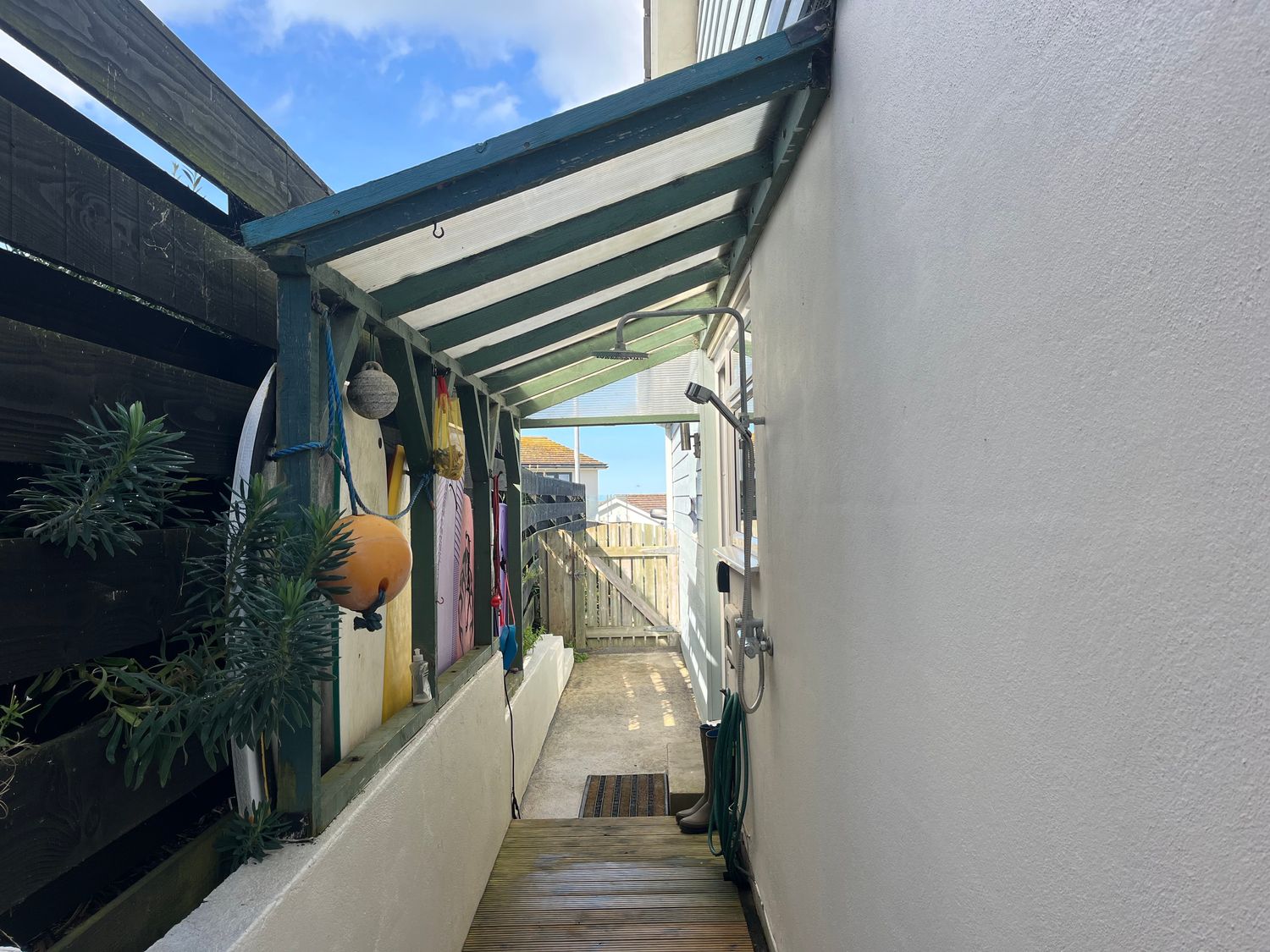 A narrow outdoor shower area with surfboards hanging and a wooden gate at Atlantis in Polzeath