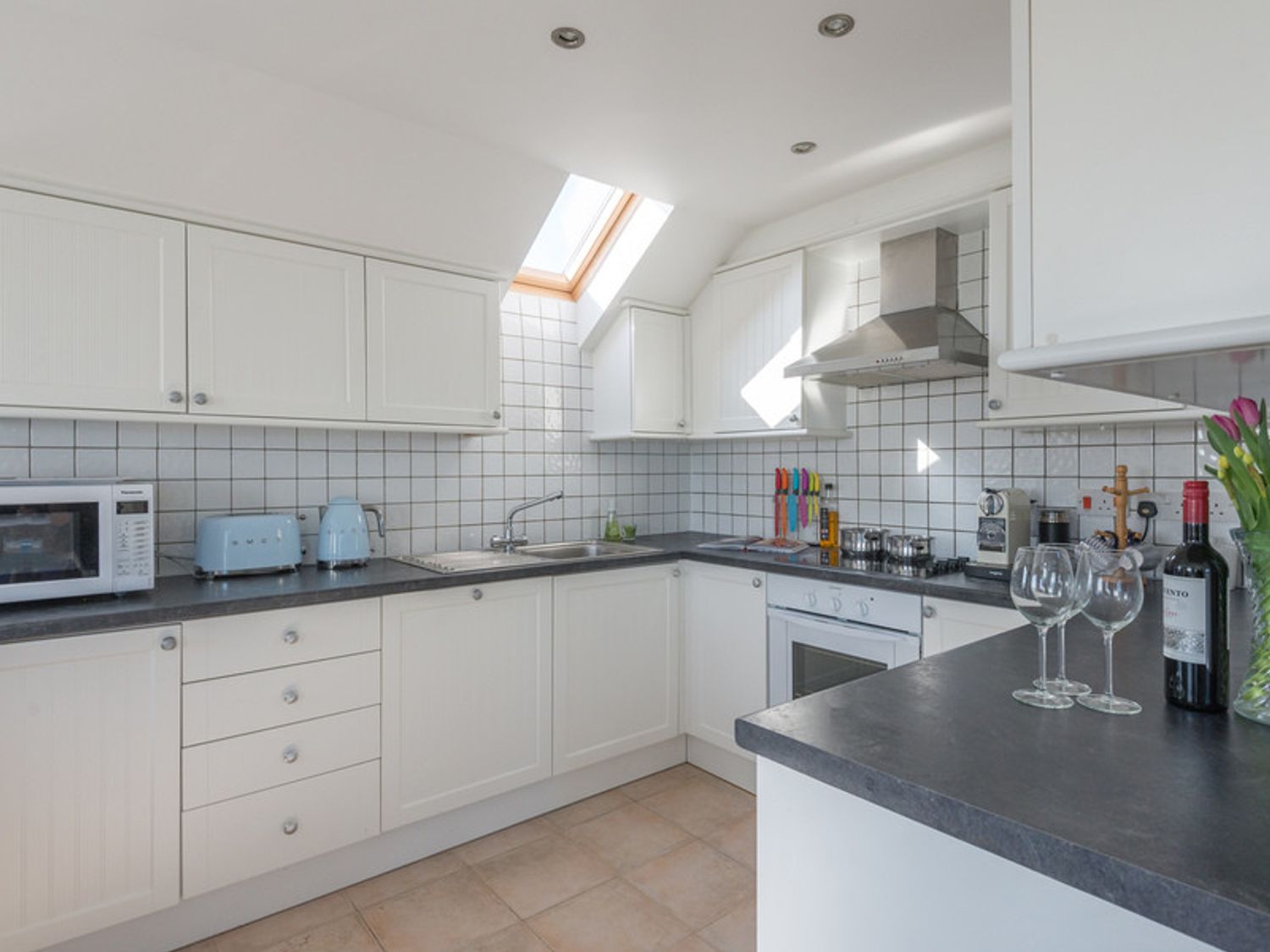 A kitchen with white cabinets black countertops a microwave toaster kettle stove oven and a skylight at Polmorla in Polzeath