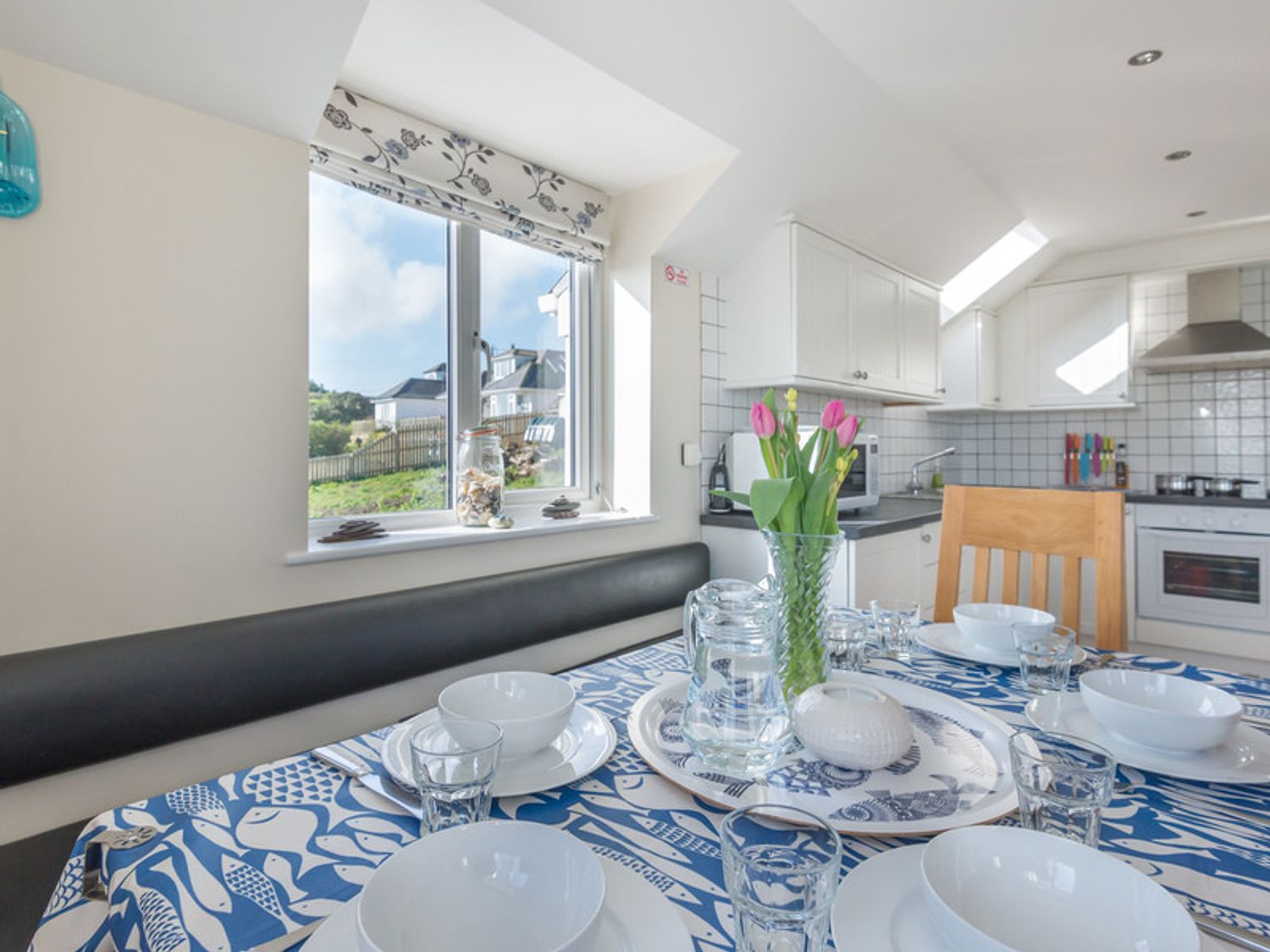 Dining table set with white bowls glasses and a vase of pink flowers in a kitchen at Polmorla in Polzeath