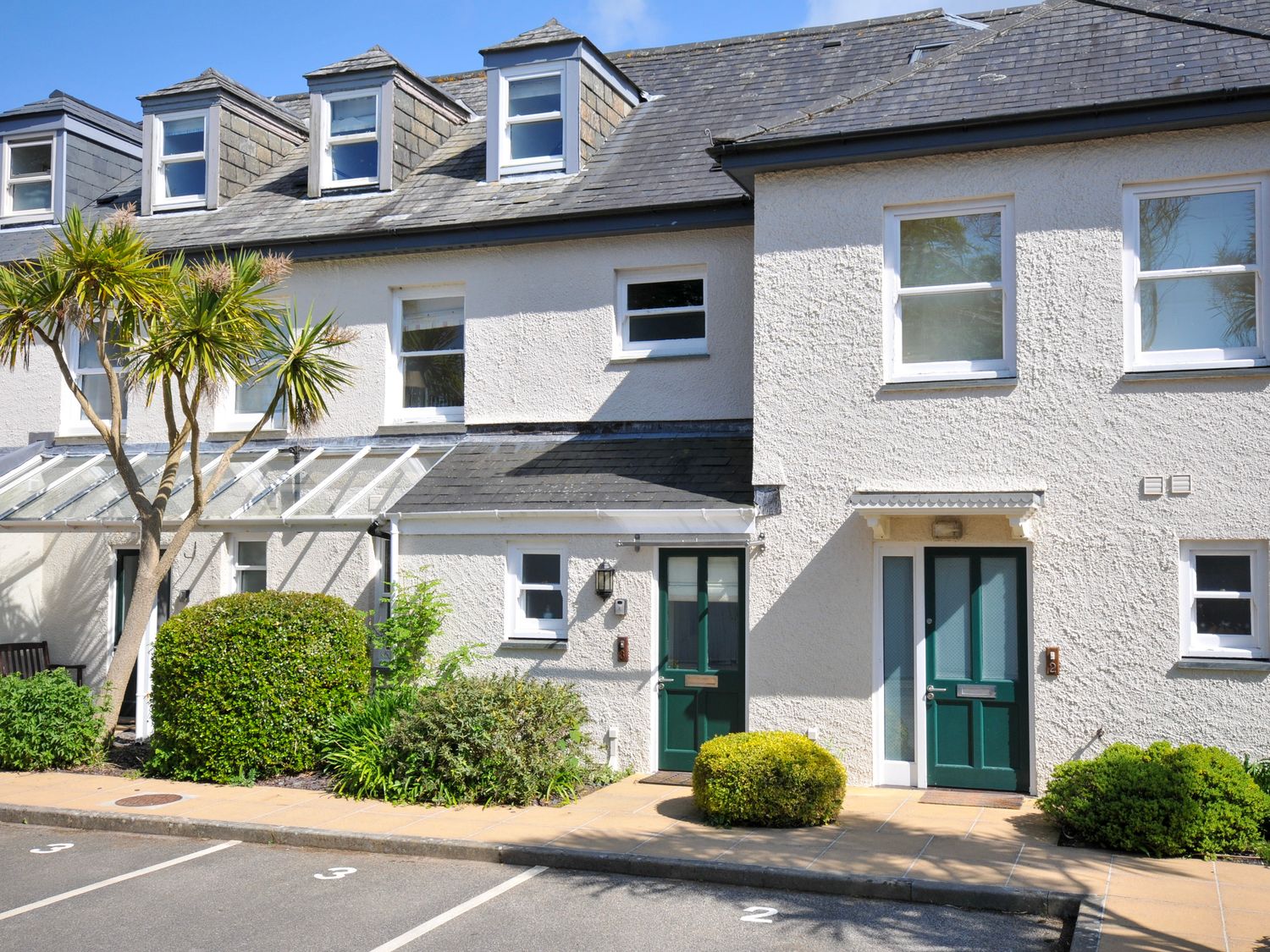A row of white townhouses with green doors and numbered parking spaces in front at Lowenna Manor 3 in Rock