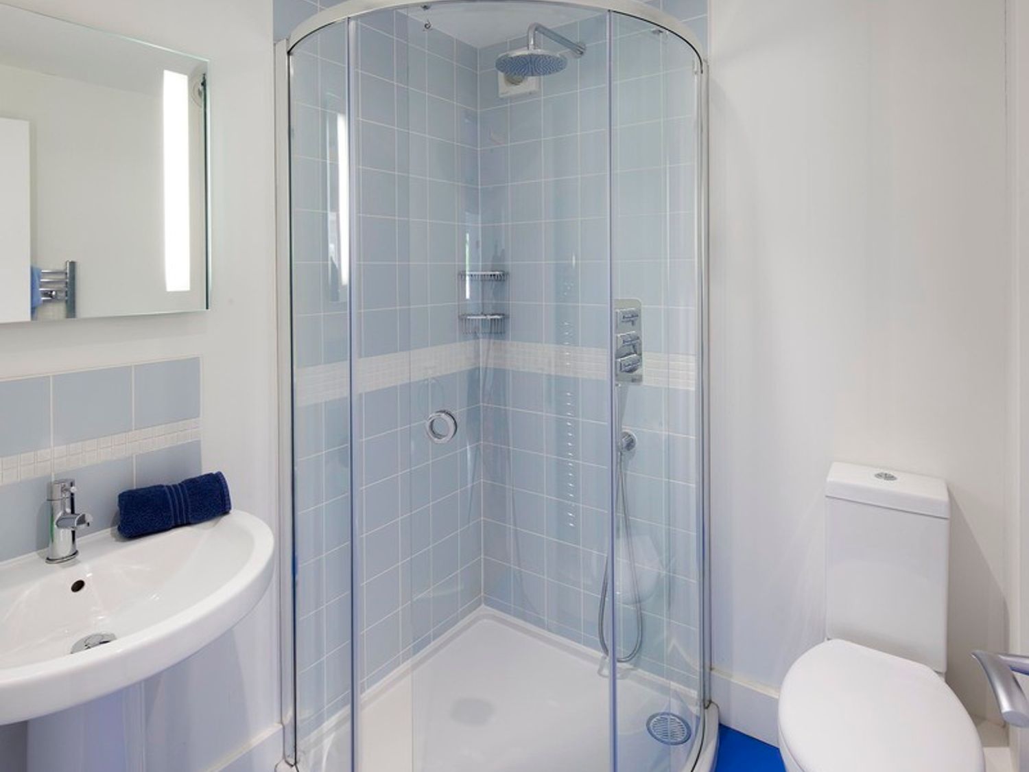 A bathroom with a curved glass shower cubicle a white sink with a blue towel and a toilet at Cherrytrees in Rock