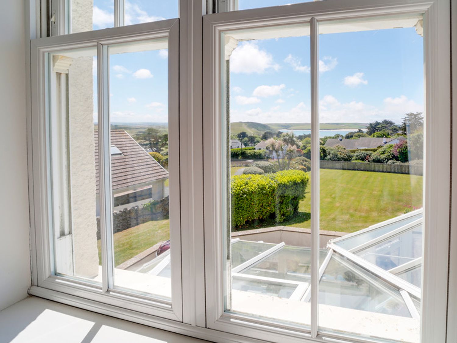 A view through a white framed window of a garden with trimmed hedges and houses beyond at The Haven in Daymer Bay
