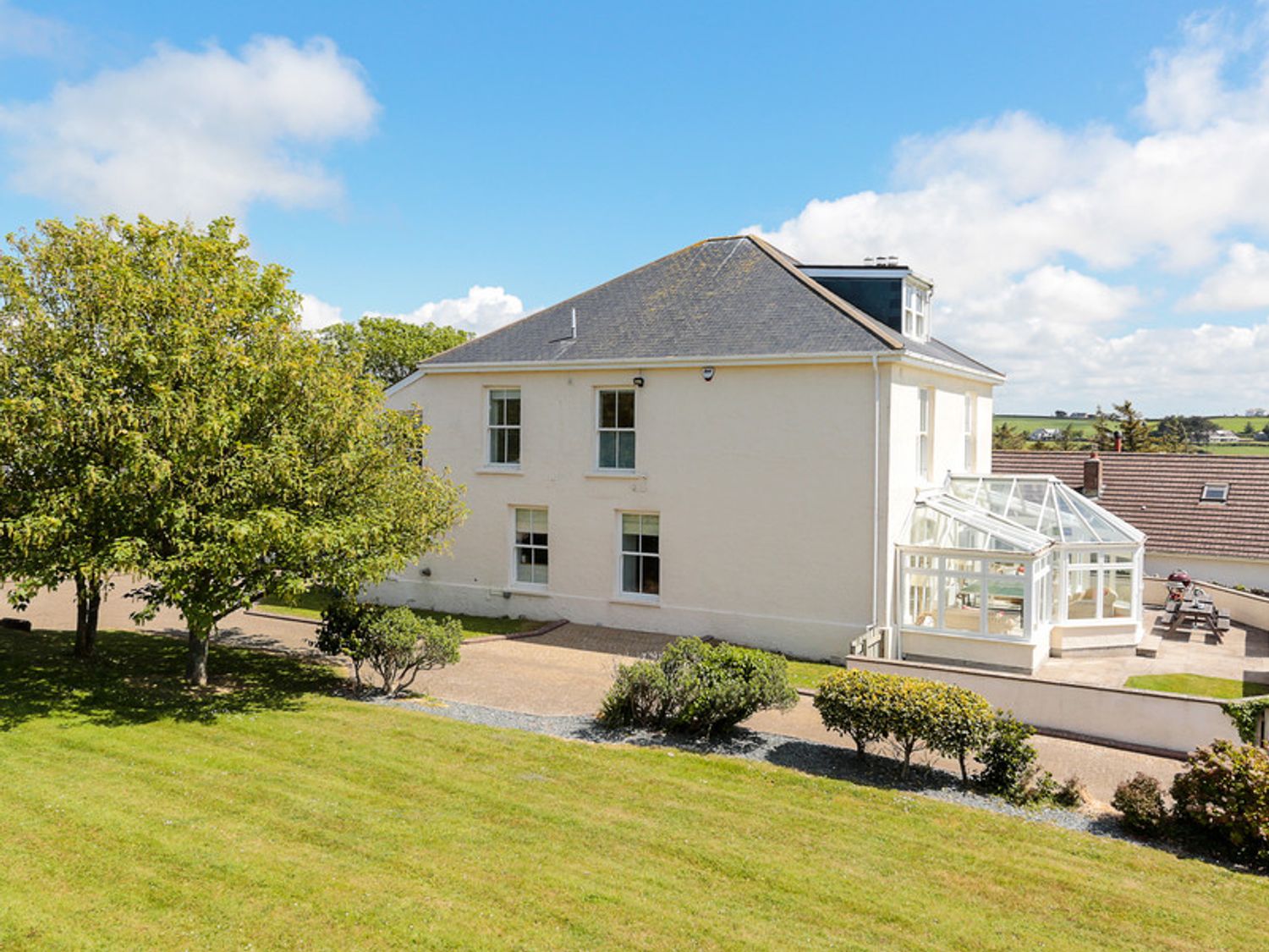 A two-story house with a glass conservatory surrounded by trees and shrubs at The Haven in Daymer Bay