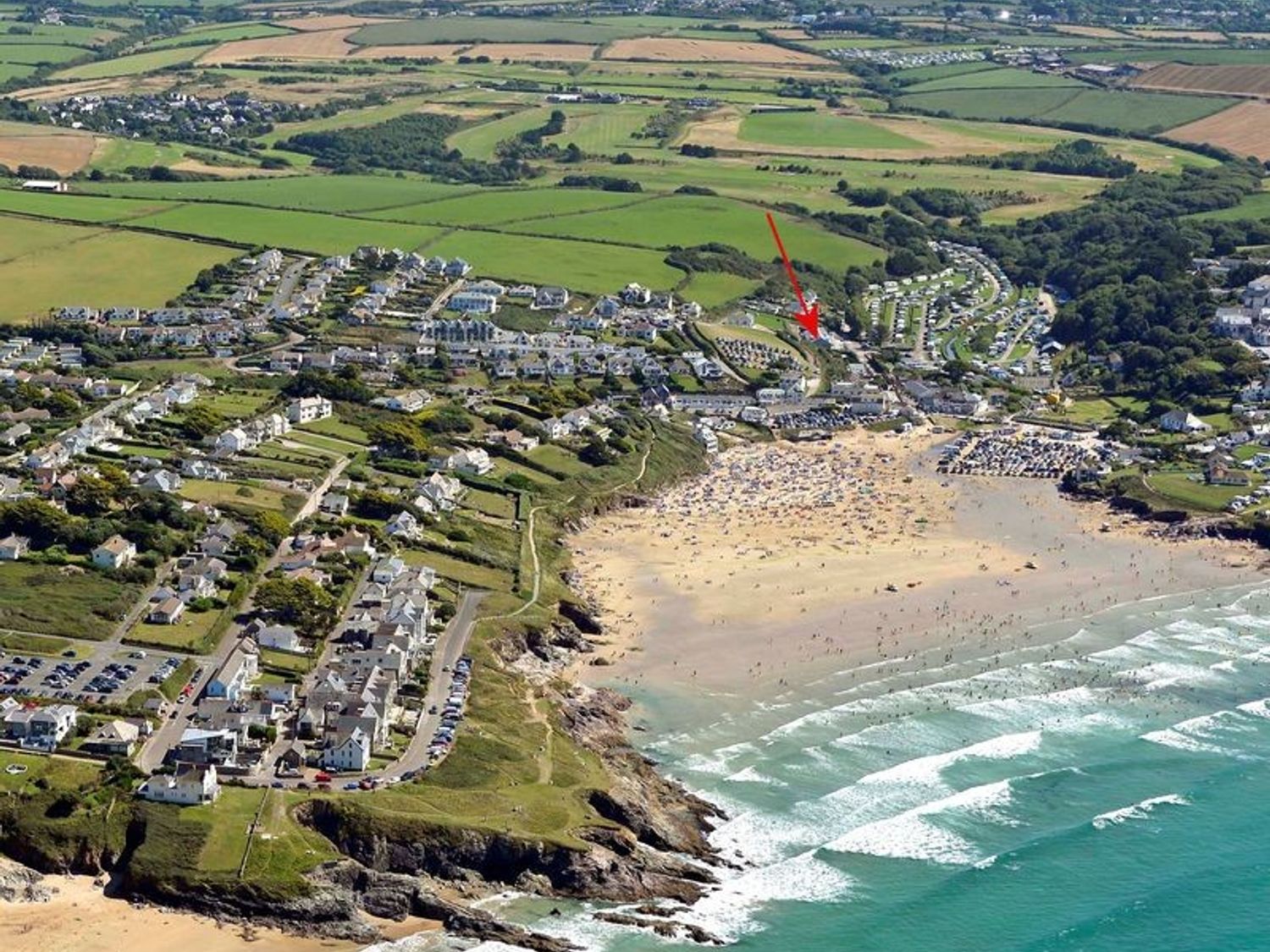 An aerial view of a coastal town with a beach fields houses and roads at Pendaveli in Polzeath