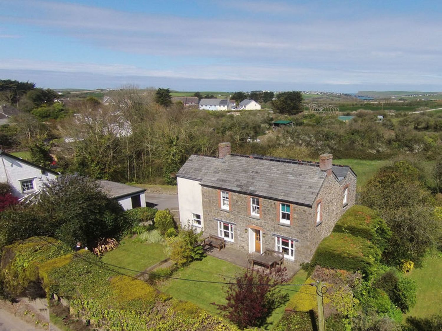 A stone house with a front garden and hedges surrounded by trees with other houses in the distance at Conifers in Rock