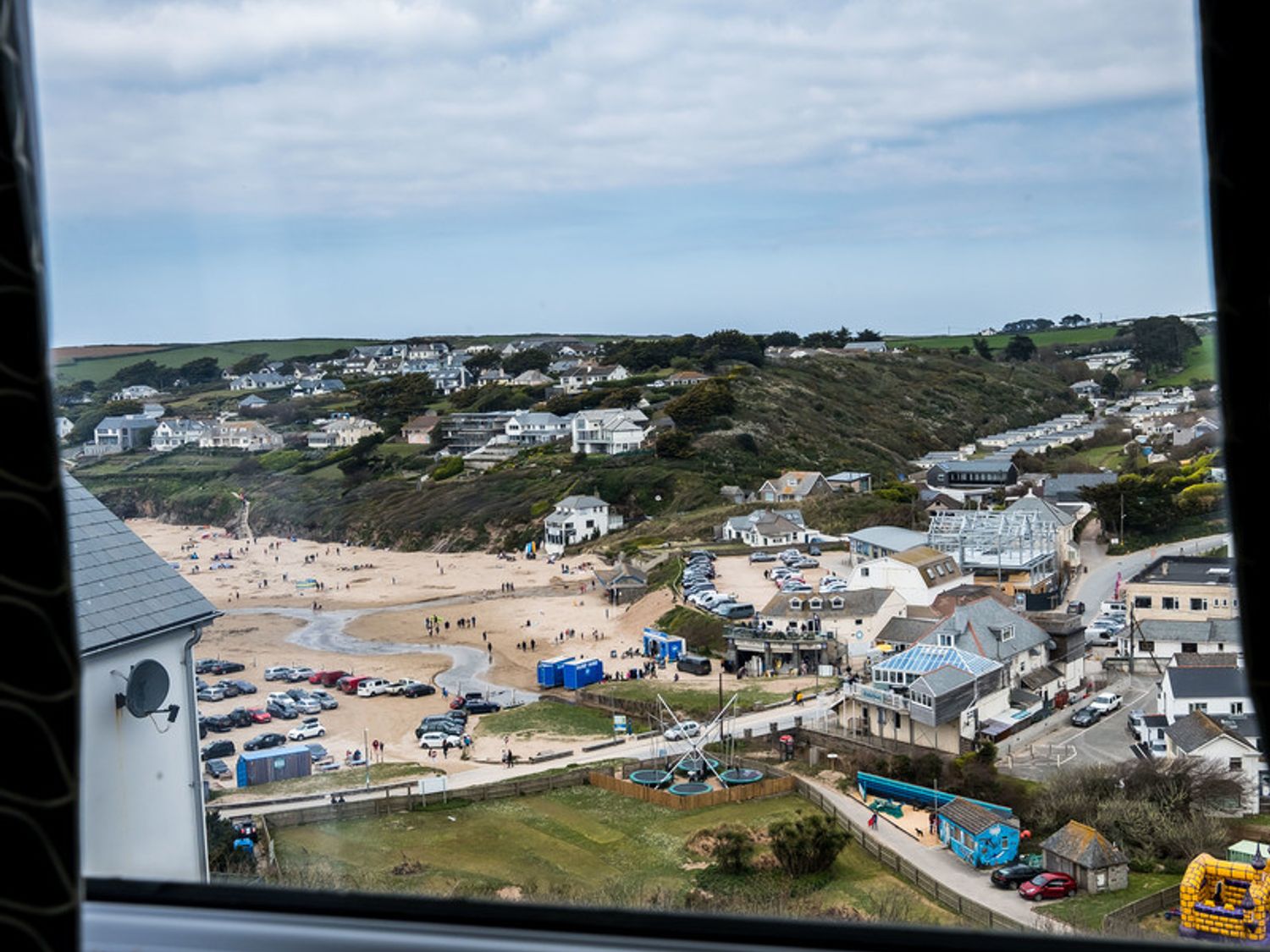 A coastal village with houses near a sandy beach and parked cars at Pinewood 14 in Polzeath