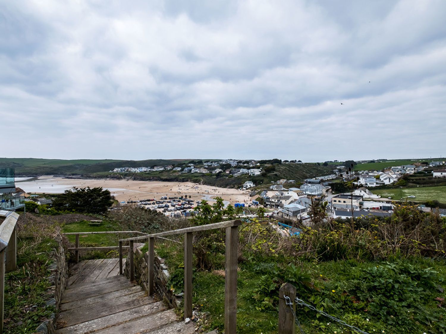 A view of a beach town with a sandy beach and houses seen from a wooden staircase on a grassy hill at Pinewood 14 Polzeath