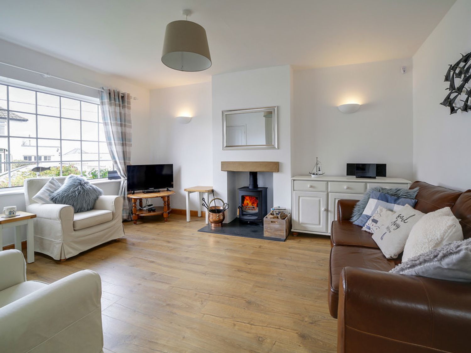 A living room with armchairs a leather sofa television and a wood burning stove at Little Sark in Port Isaac