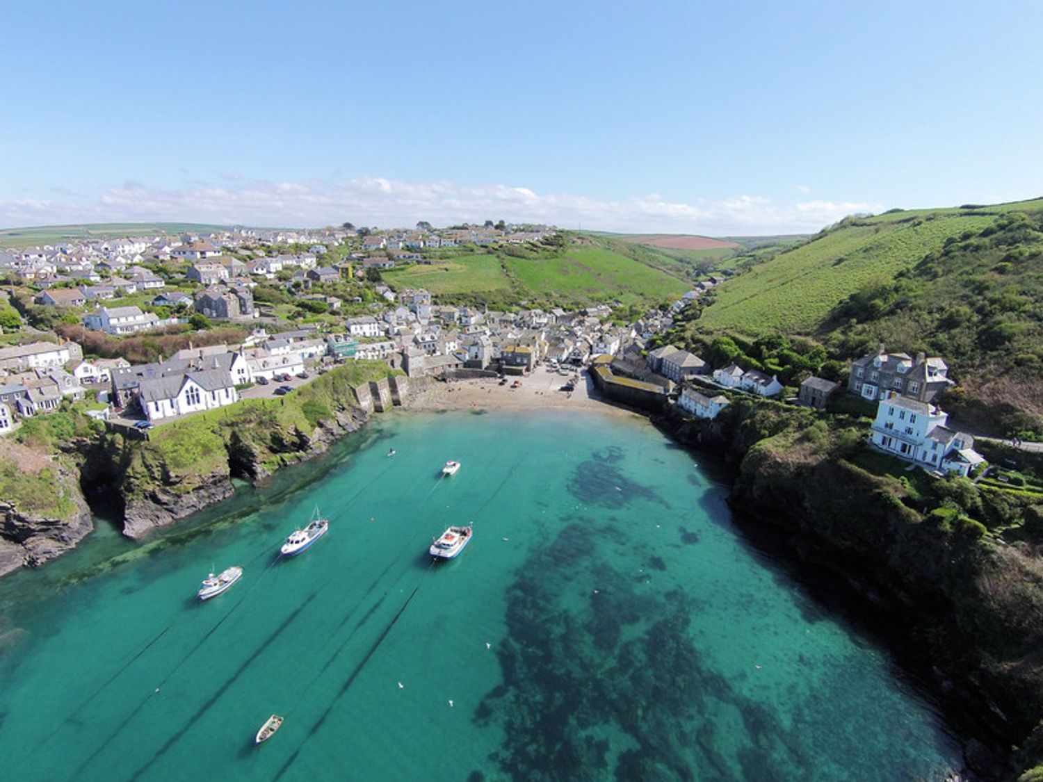 A coastal village with houses on green hills and boats in clear water at Little Sark in Port Isaac