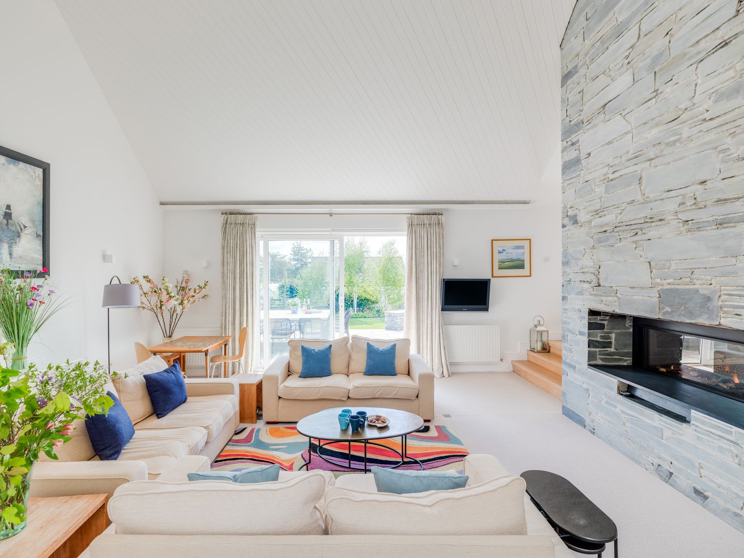 A living room with beige sofas blue pillows a stone fireplace and a sliding glass door at Landers Field in Rock