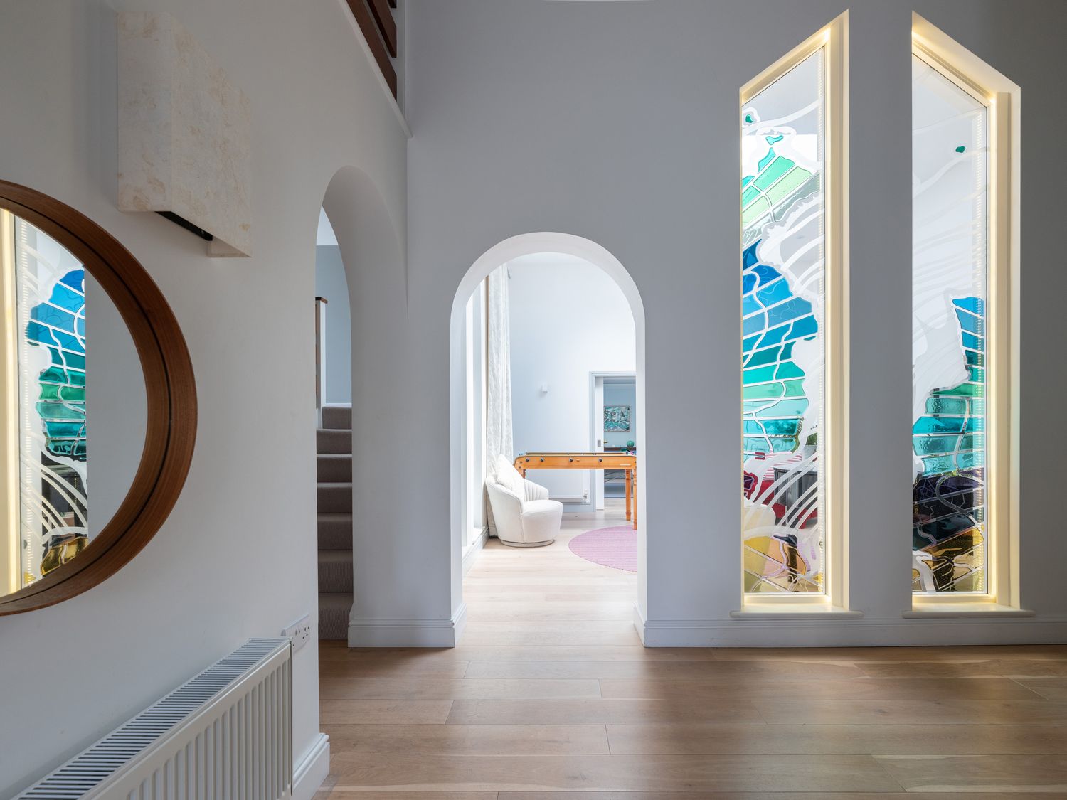 A hall with wooden floor a round mirror and radiator with archways leading to a room with a chair and foosball table at Landers Field in Rock