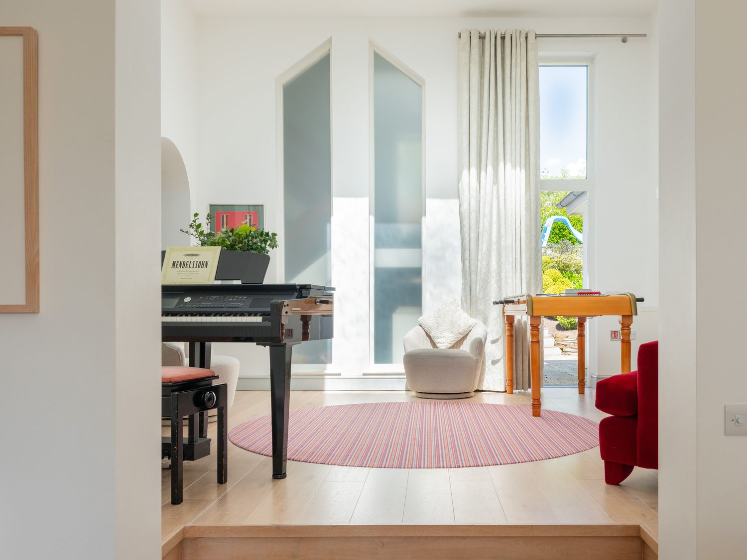 A room with a piano a round striped rug a beige armchair a foosball table and a red armchair at Landers Field in Rock