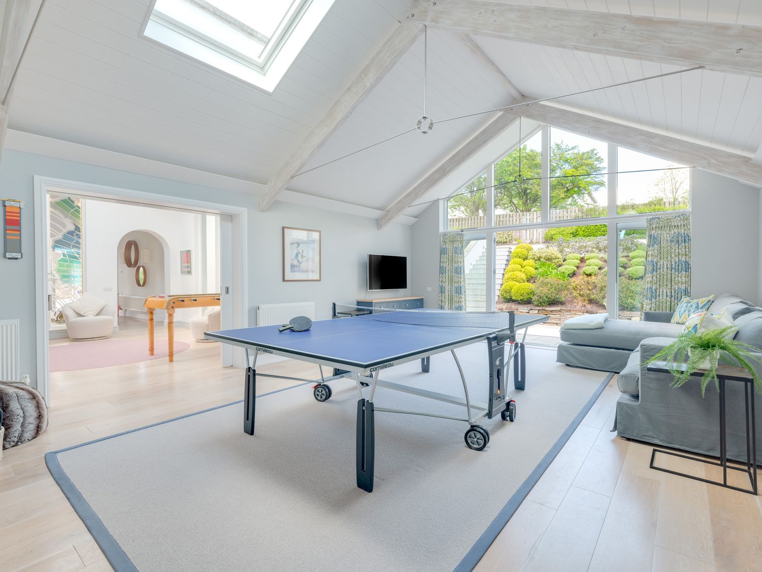 A room with a ping pong table, a sectional sofa, a television, and large windows overlooking a garden at Landers Field in Rock