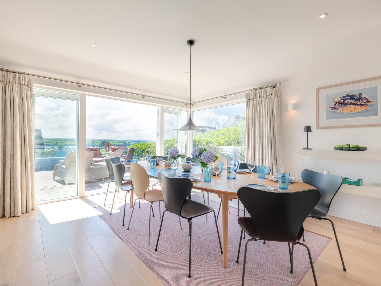 A dining room with a wooden table set with plates glasses and flowers and black and beige chairs with glass doors leading outside at Landers Field in Rock