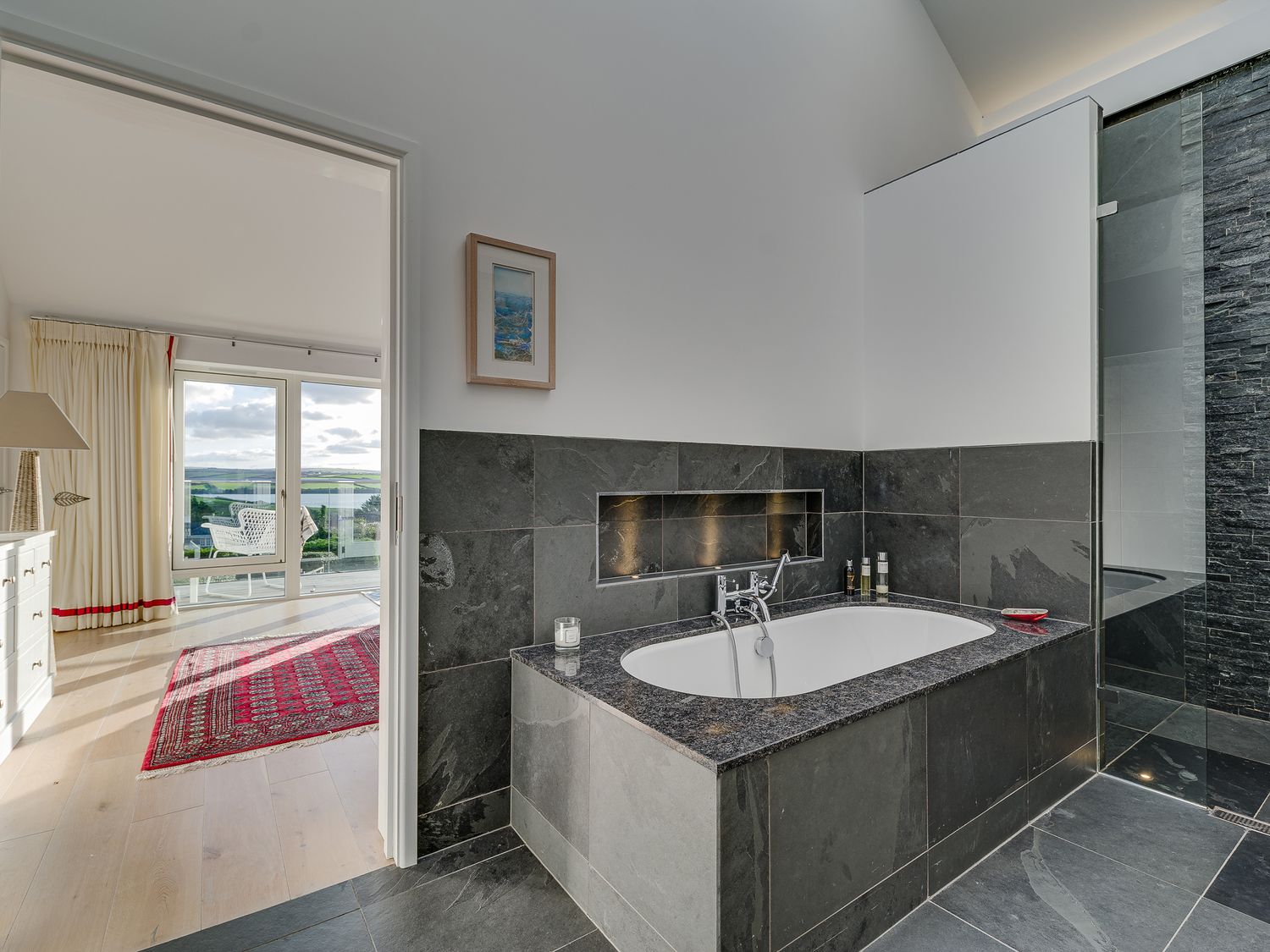 A bathroom with a bathtub and shower next to a room with a red rug and large windows at Landers Field in Rock