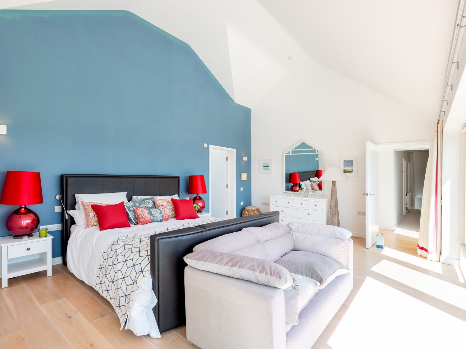 A bedroom with a blue accent wall a bed with red lamps on white nightstands and a gray couch at Landers Field in Rock