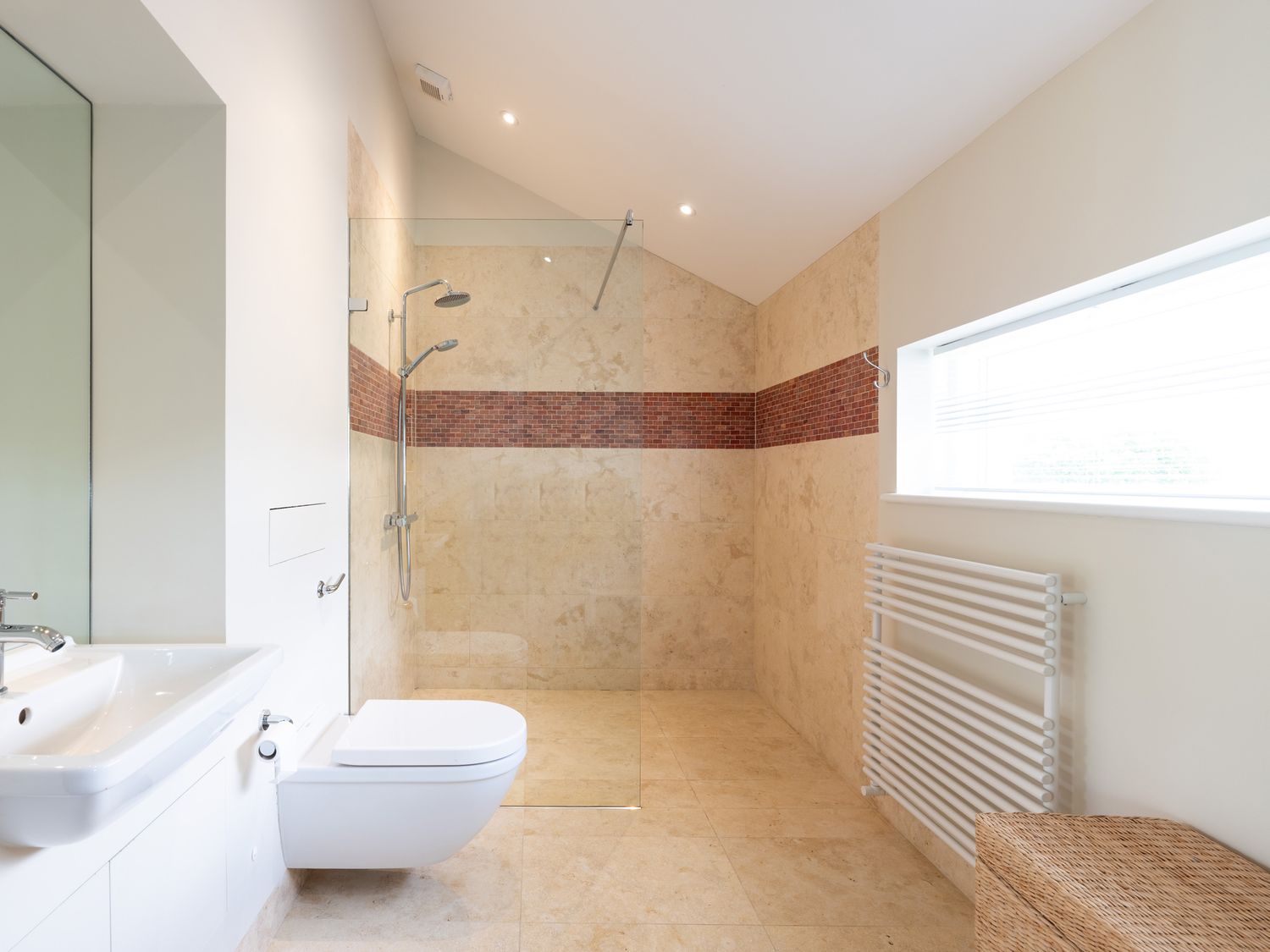 A bathroom with a wall-mounted toilet a sink a walk-in shower with two showerheads a window and a wicker basket at Landers Field in Rock