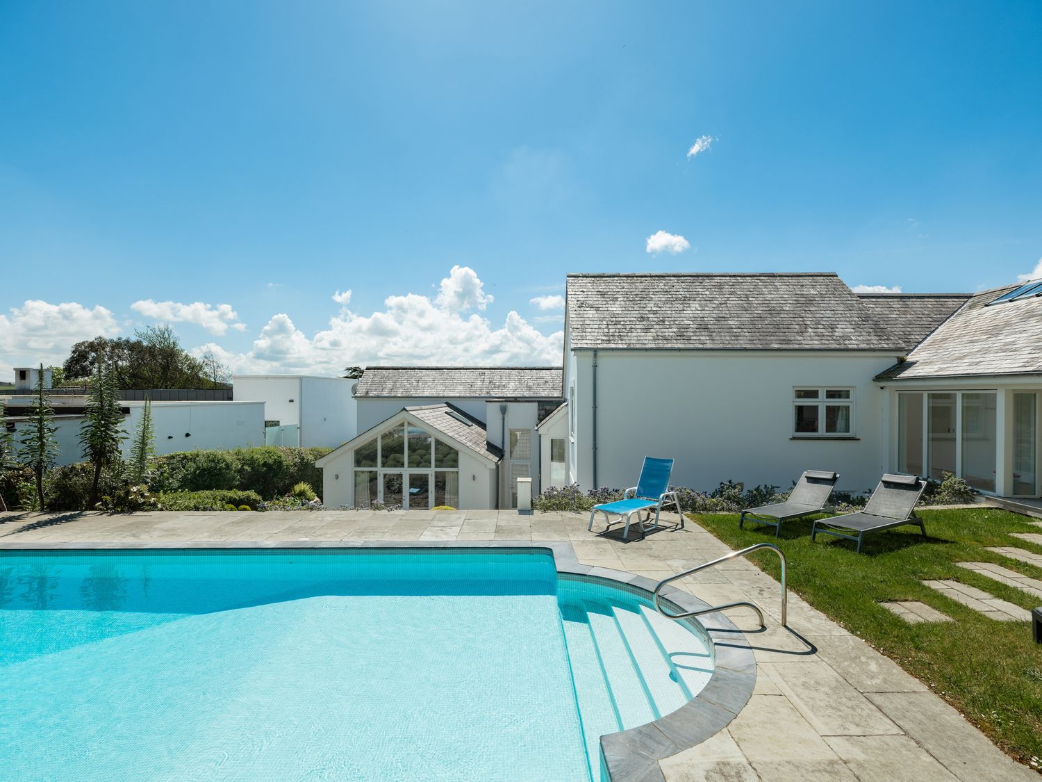 An outdoor swimming pool with steps and lounge chairs near a white house at Landers Field in Rock