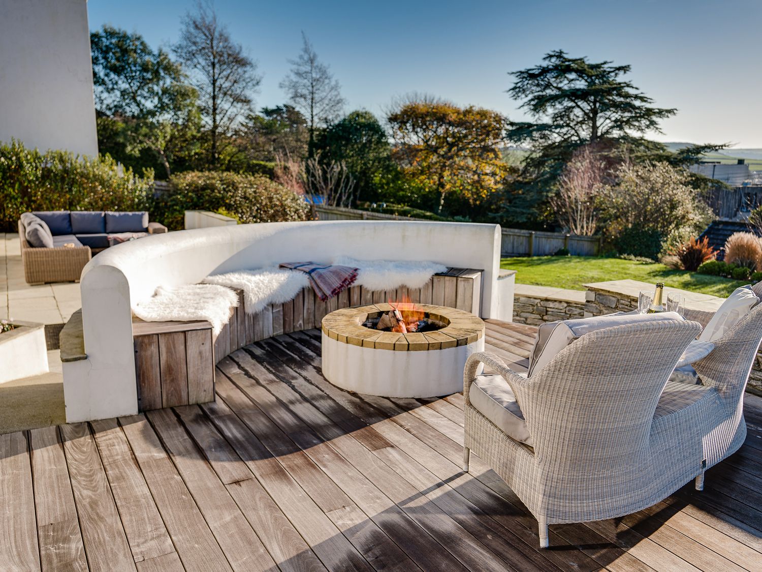 An outdoor patio with a curved bench around a fire pit and wicker chairs on a wooden deck at Landers Field in Rock