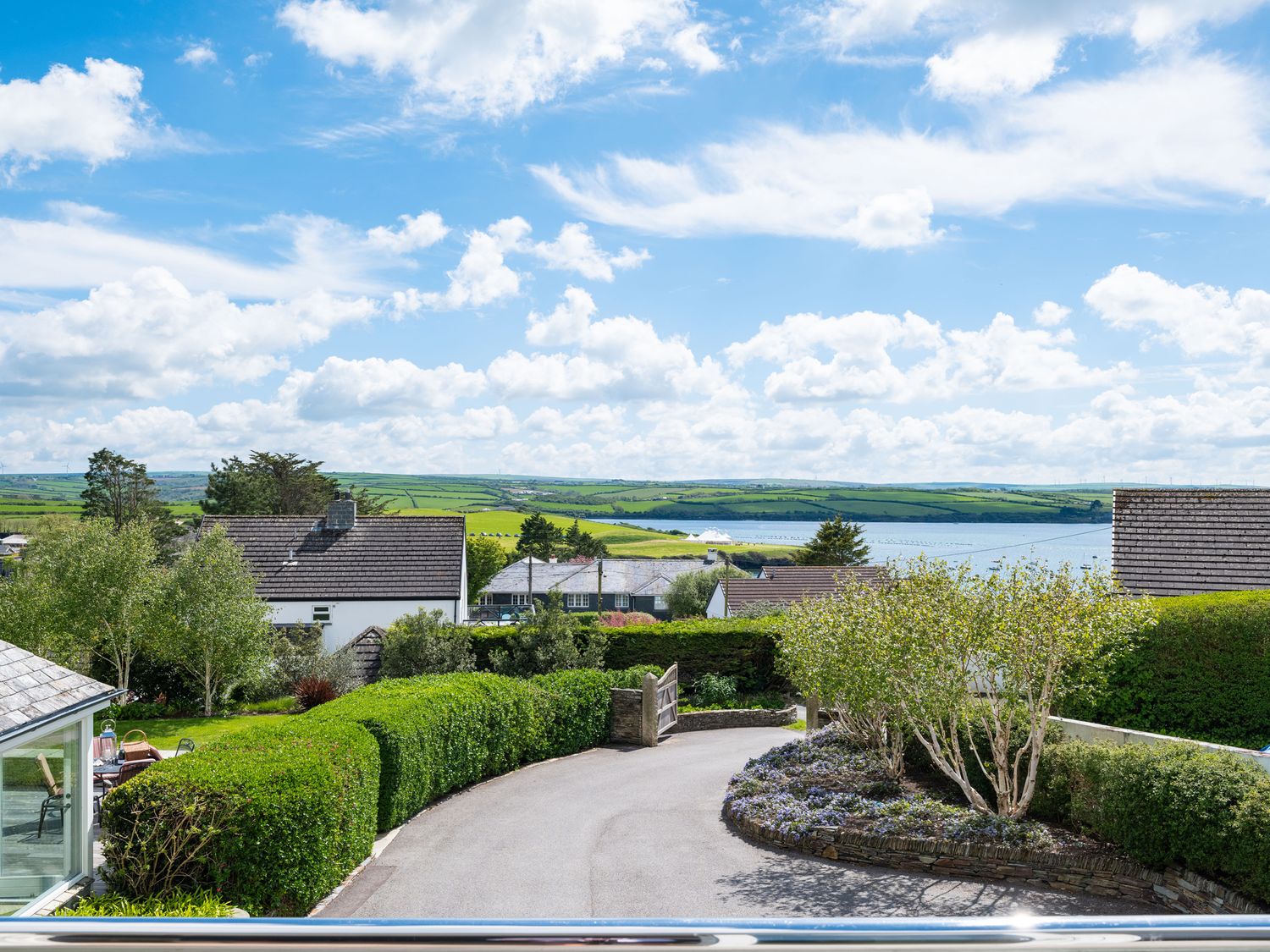 A driveway with hedges and trees leading to a gate with houses and fields in the background at Landers Field Rock