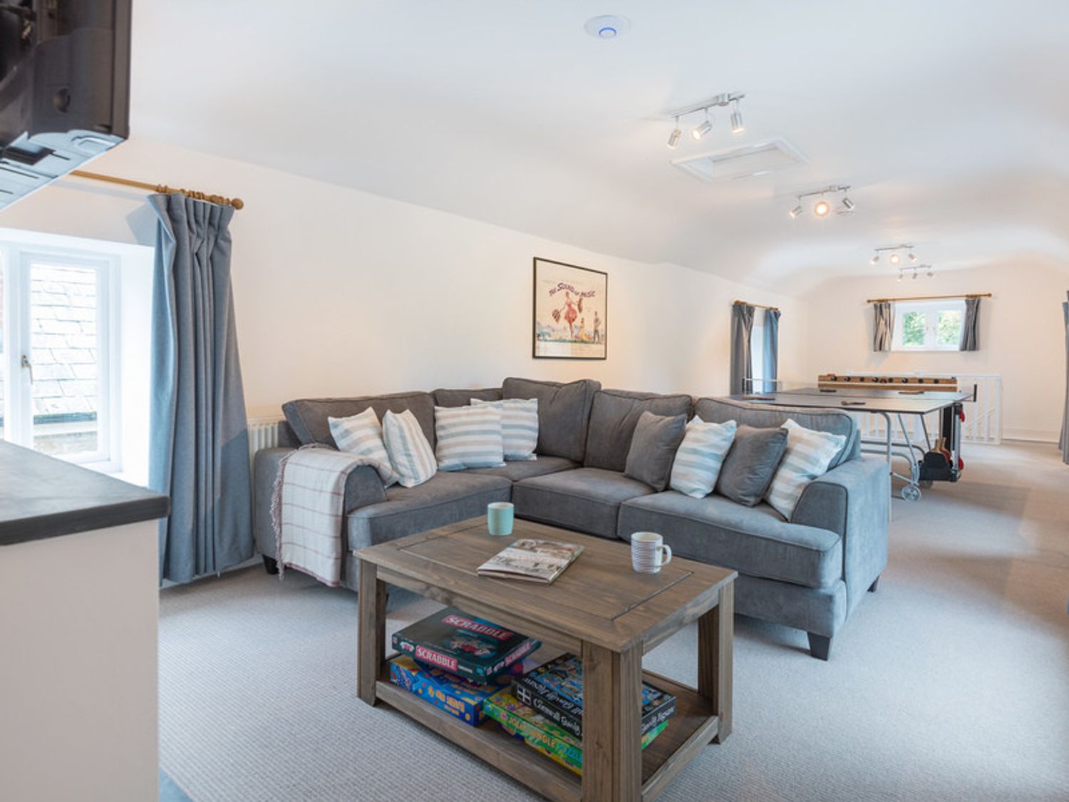 A living room with a gray sectional sofa a wooden coffee table and game boards on the lower shelf at Orchard Cottage Polzeath