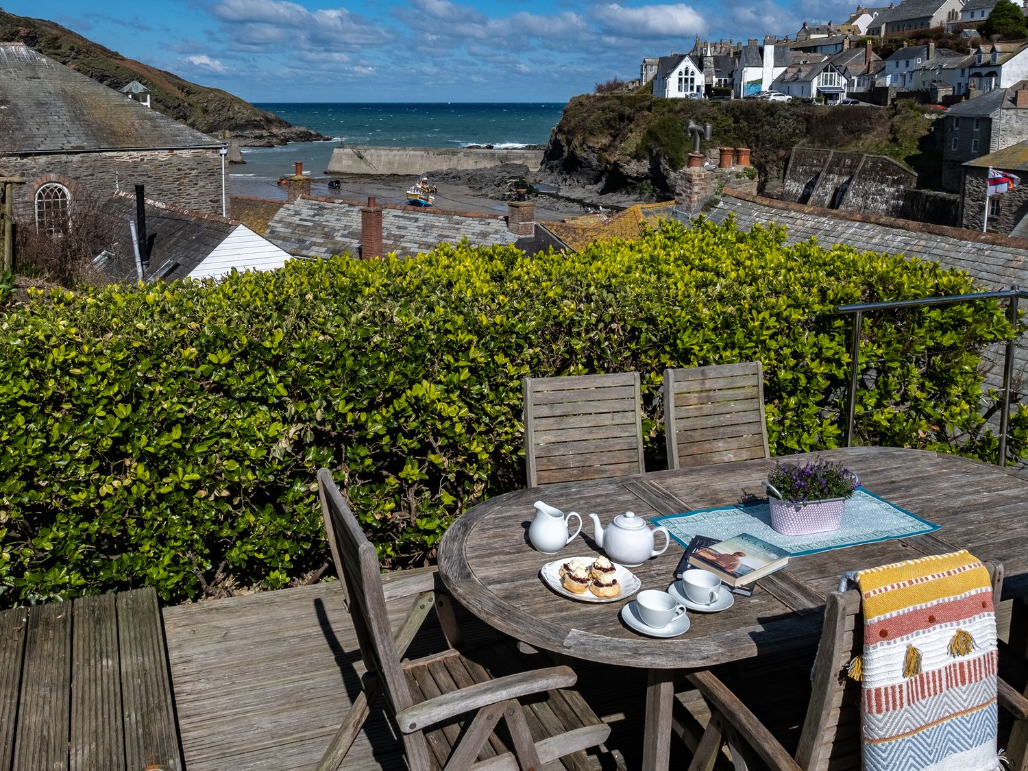 An outdoor wooden table with tea set and scones on a deck overlooking houses and the sea at Grey Roofs in Port Isaac