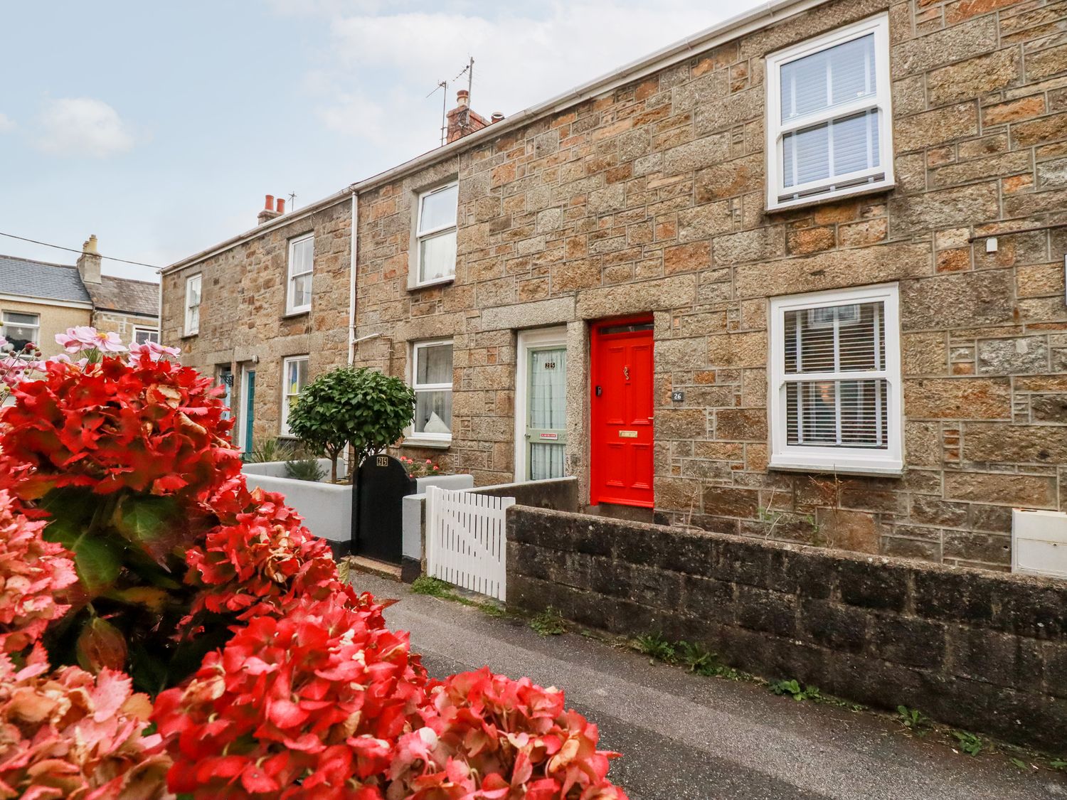 A row of stone houses with a red door and flowers in front at Pandora Cottage in Newlyn