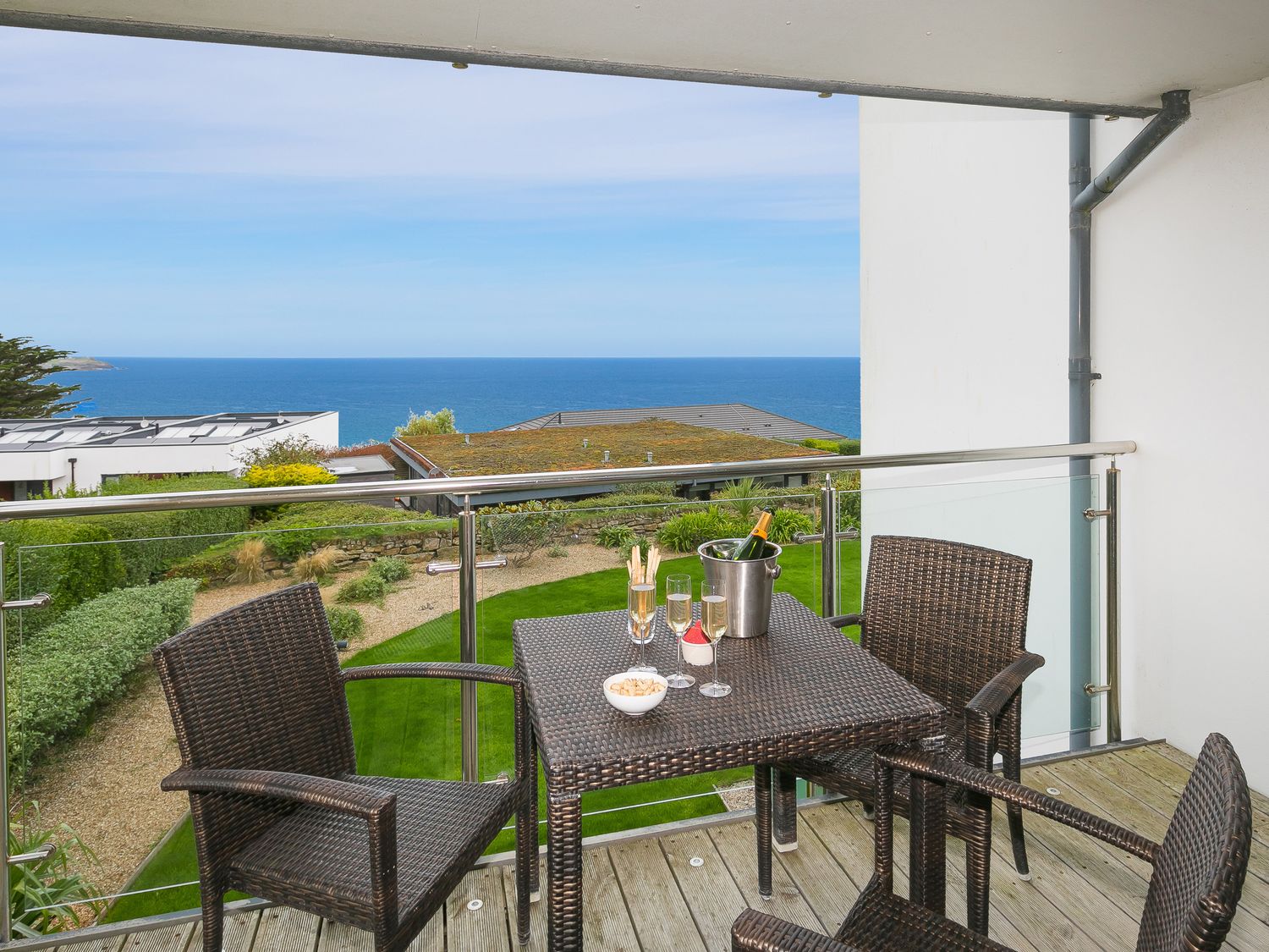 A balcony with a table and four chairs with champagne glasses and a bottle overlooking the sea at Far Cliffs in Carbis Bay