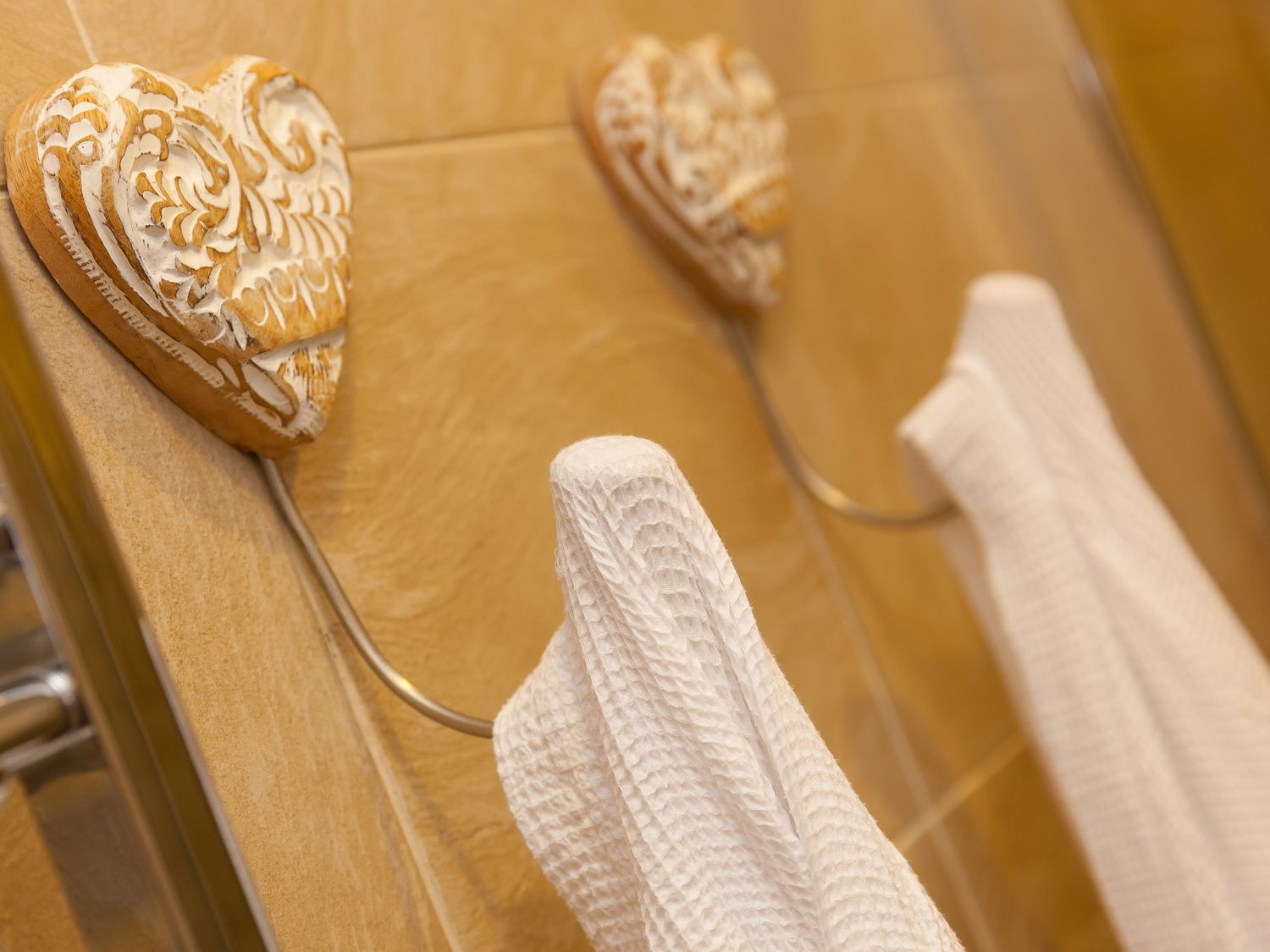 Two decorative heart shaped wall hooks holding white towels on a tiled wall at Far Cliffs in Carbis Bay