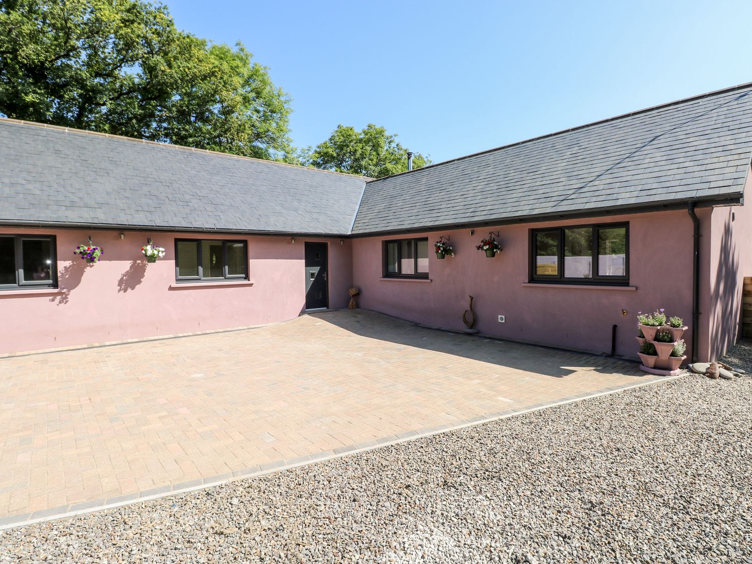 A courtyard with pink exterior walls black-framed windows hanging flower pots and a tiled driveway at 1 The Warren Robeston Wathen near Narberth