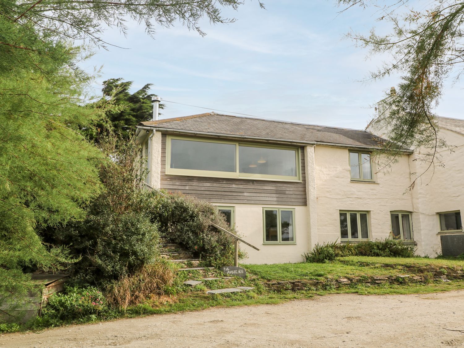 A building with multiple windows surrounded by trees and shrubs at Porth Farm Annexe in Mawgan Porth