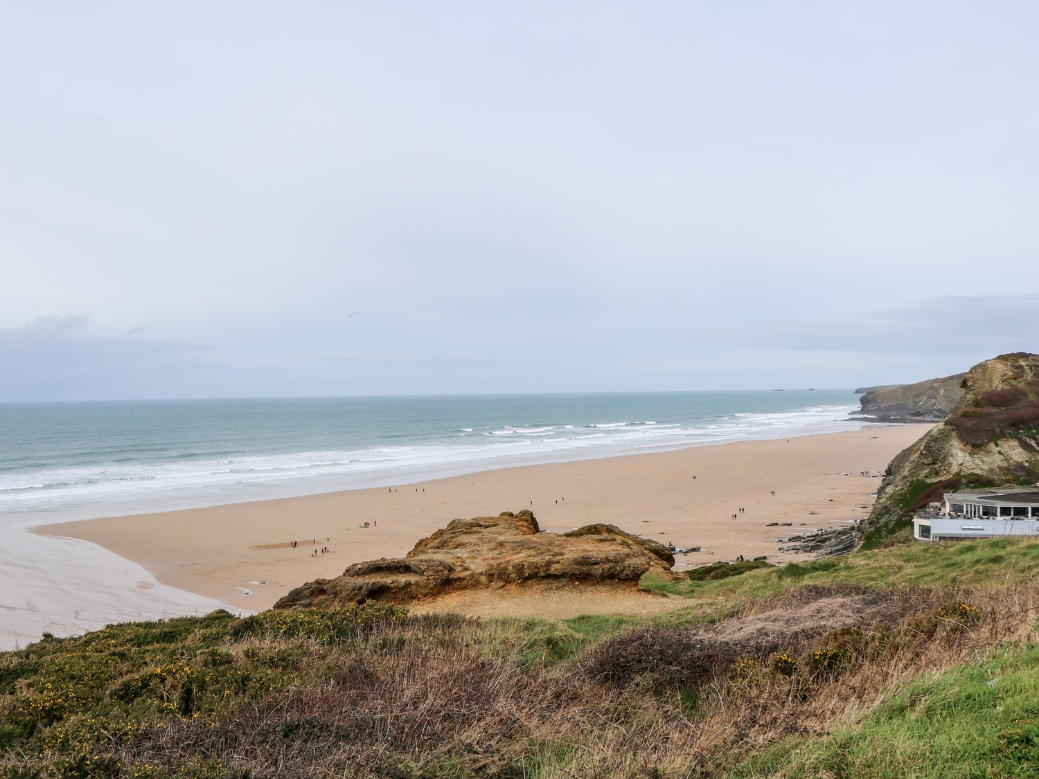 A sandy beach with ocean waves and rocky cliffs with some vegetation at Porth Farm Annexe in Mawgan Porth