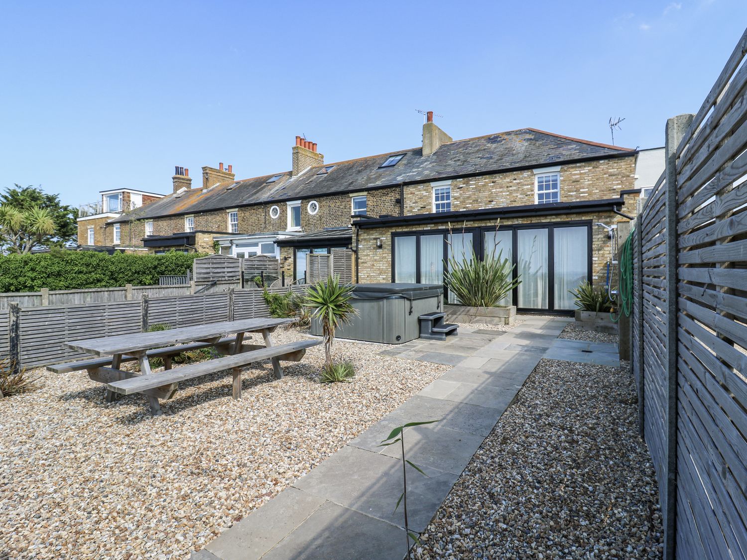 A garden with a dining table and hot tub at Coast Guard House in Swalecliffe